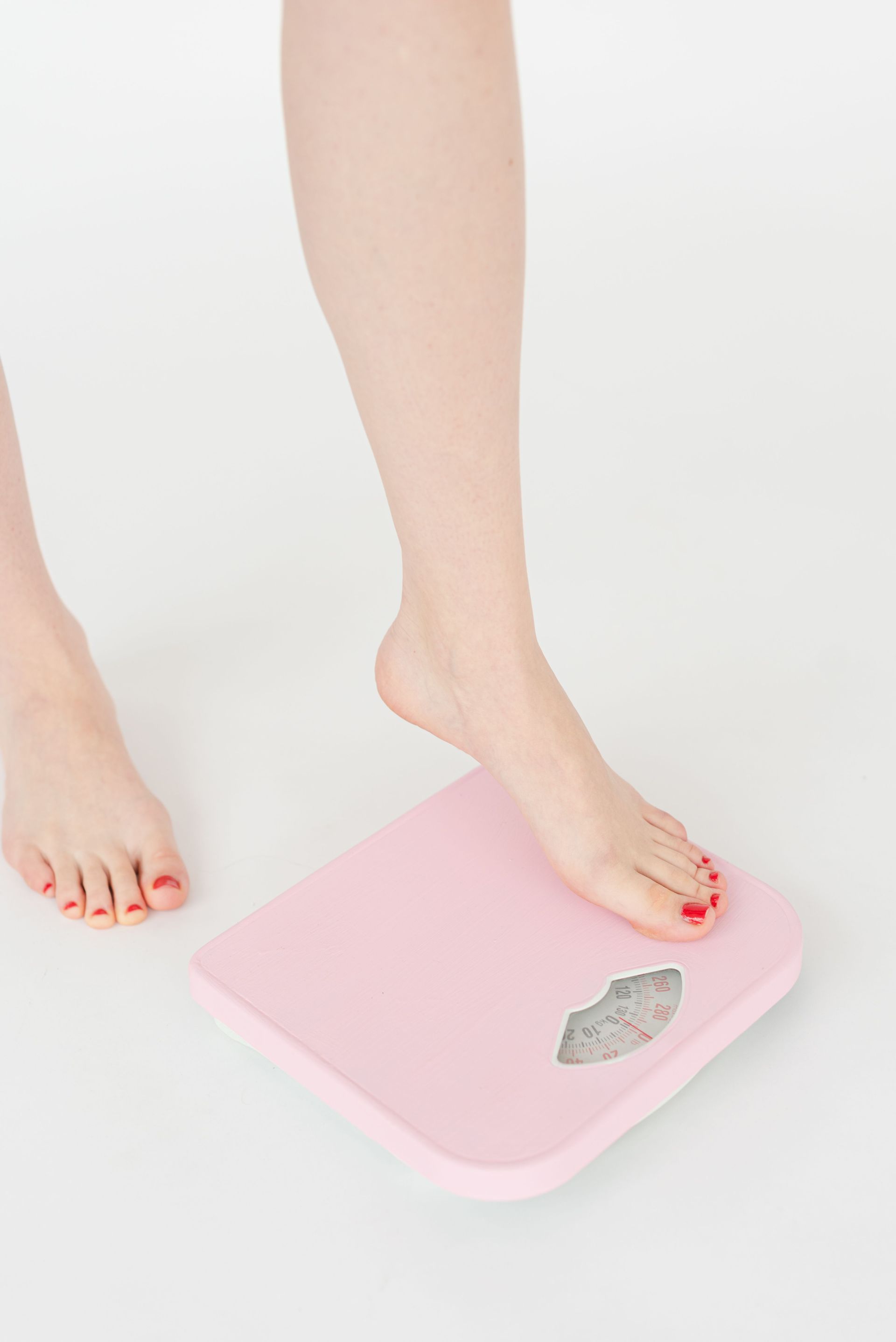 Foot on a pink bathroom scale on a white floor