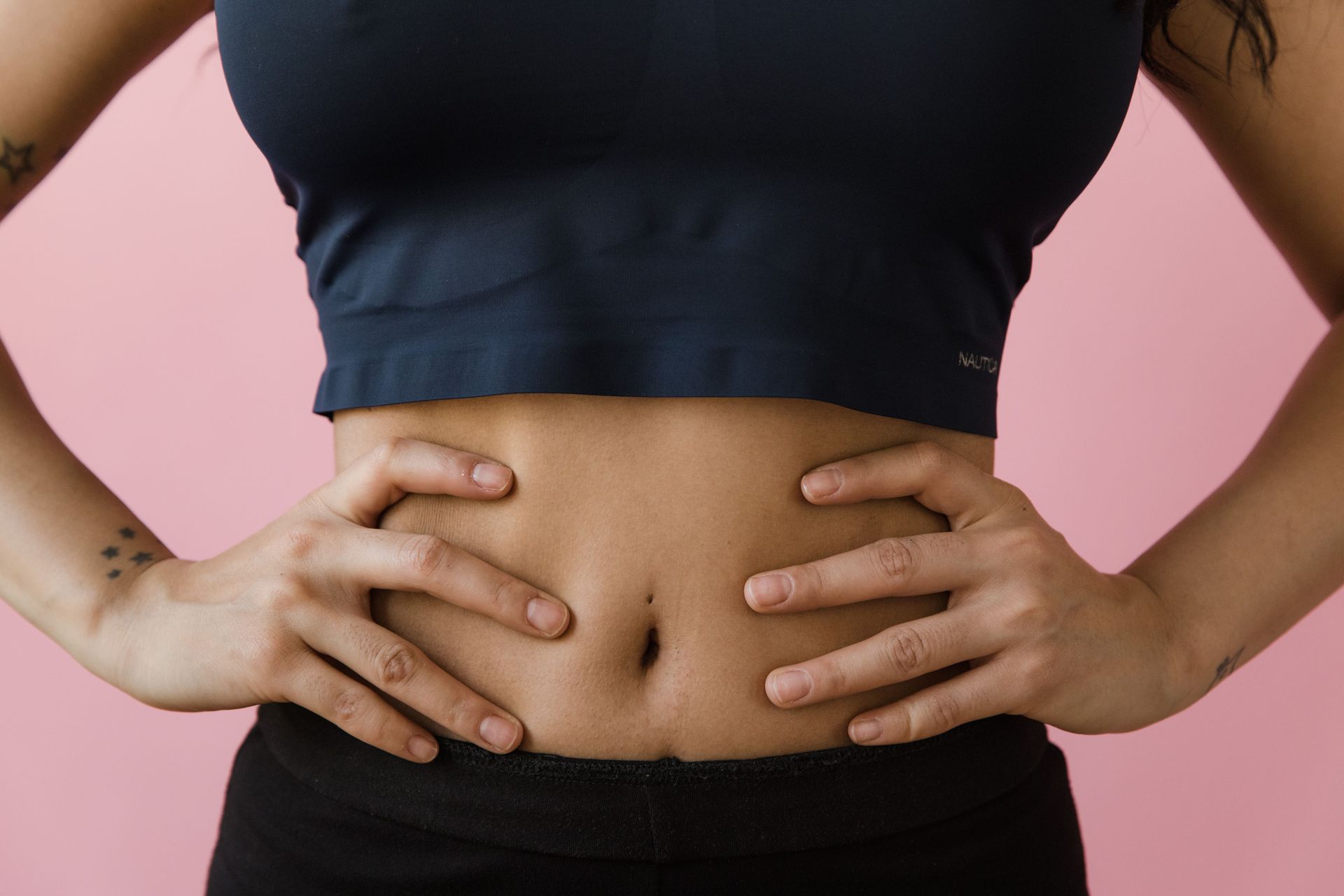 Person holding their stomach with both hands, wearing a black top against a pink background
