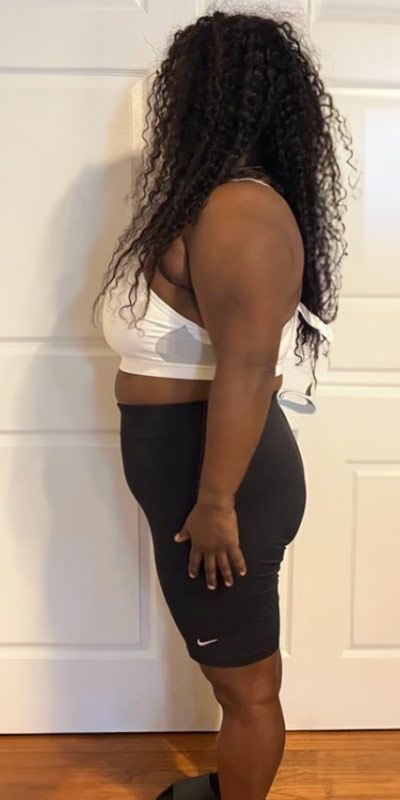 A woman in a white bra and black shorts is standing in front of a door.