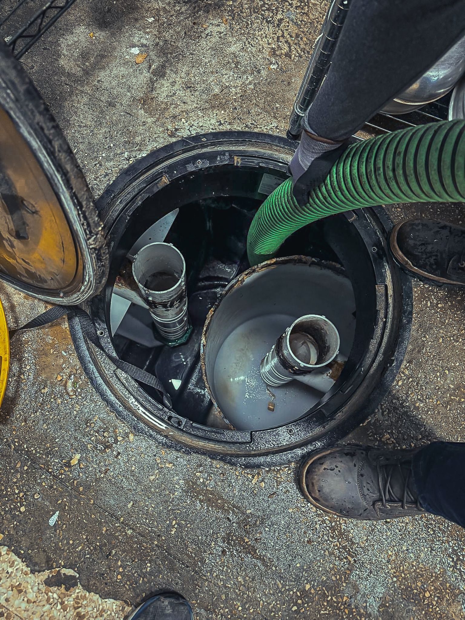 A person is pumping water into a manhole cover with a green hose.