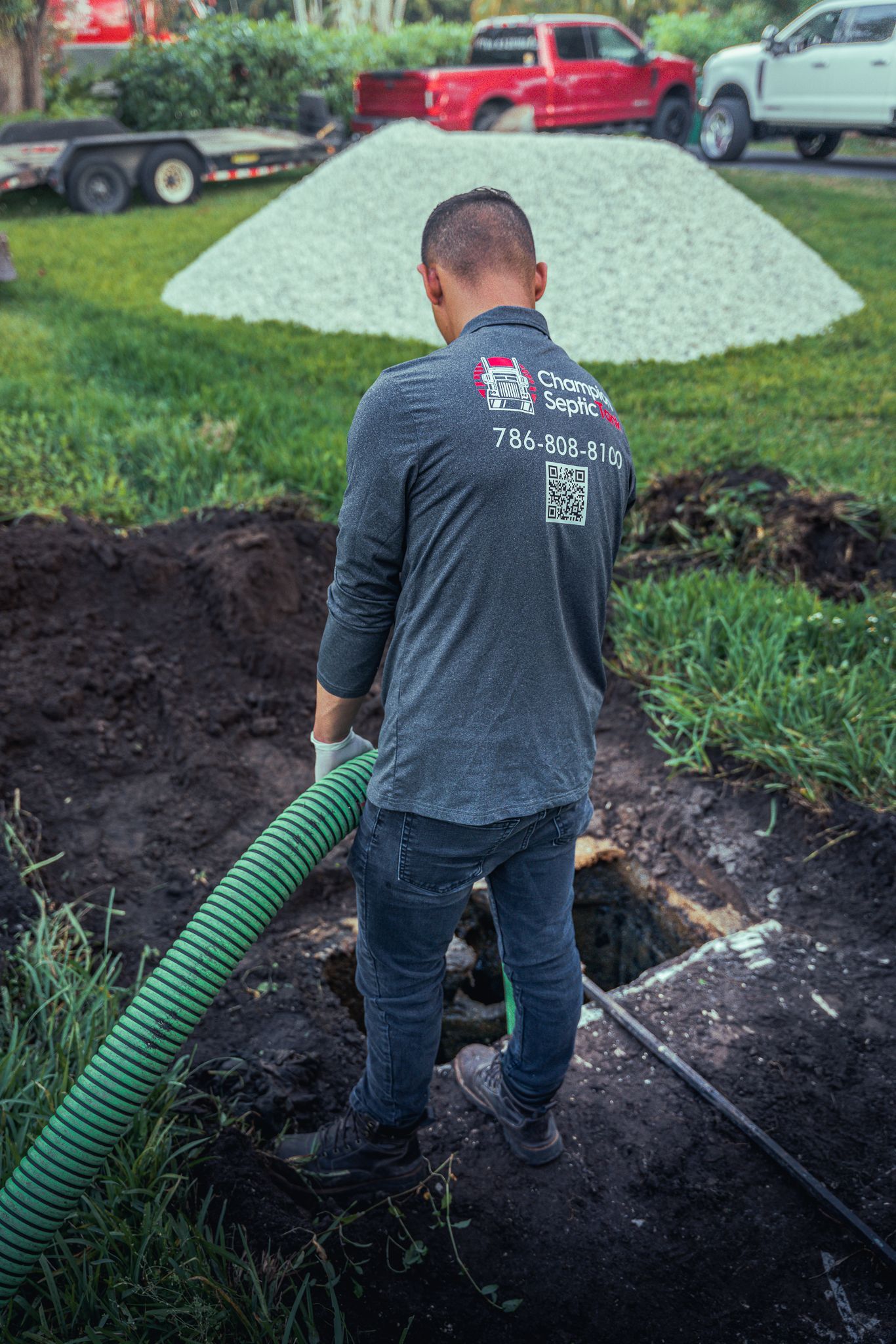 A man is standing in the dirt holding a green hose.