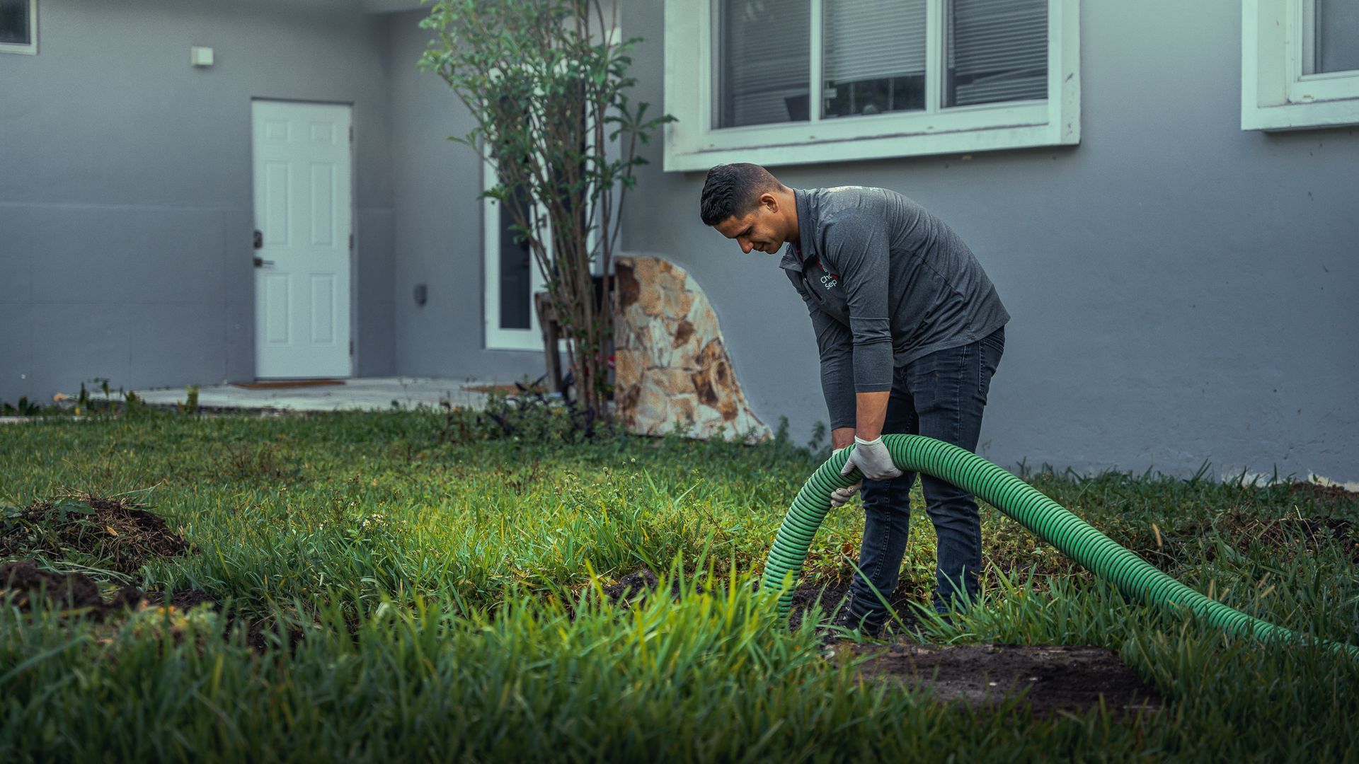 A man is using a green hose to pump water into a septic tank.