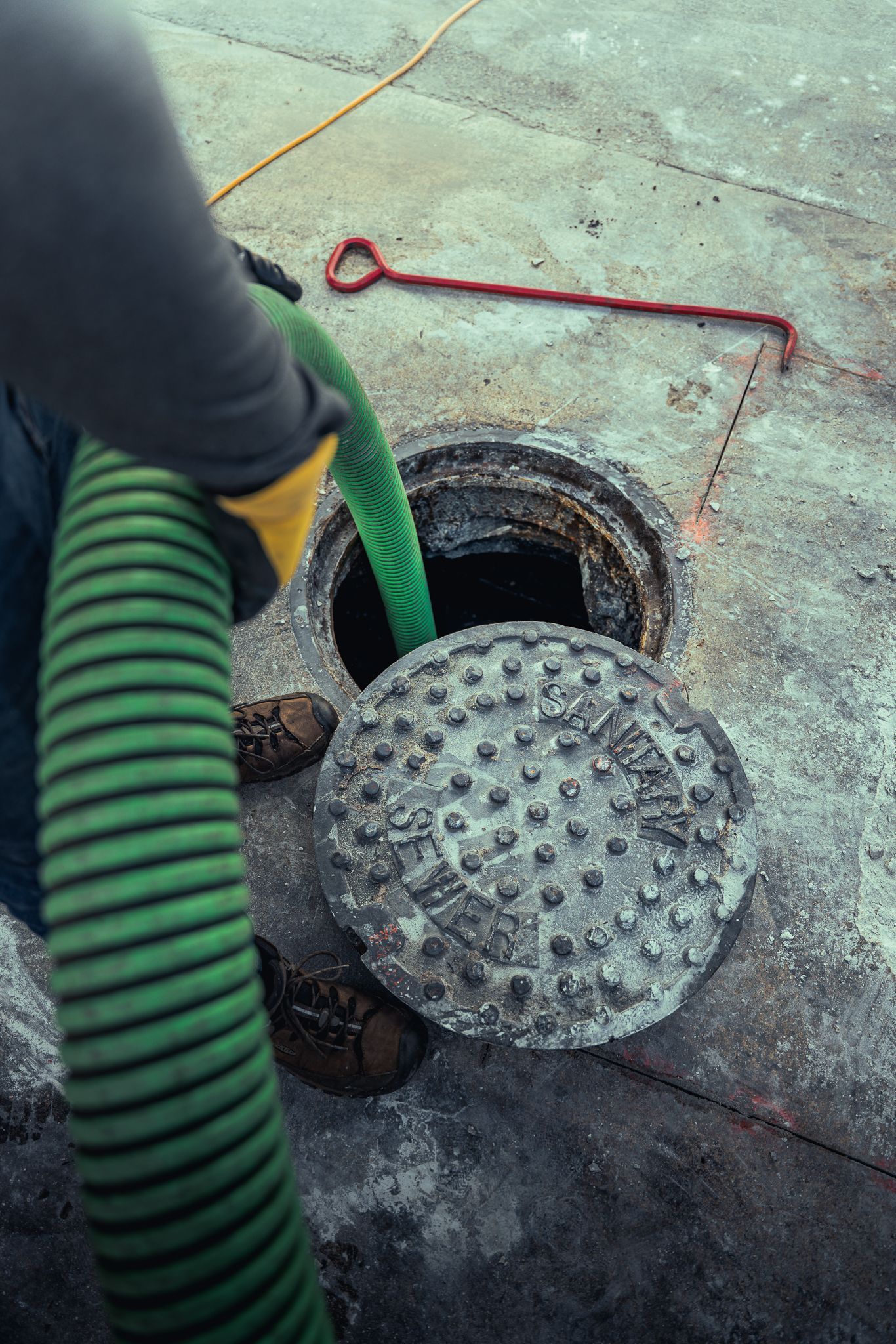 A man is pumping a green hose into a hole in the ground.