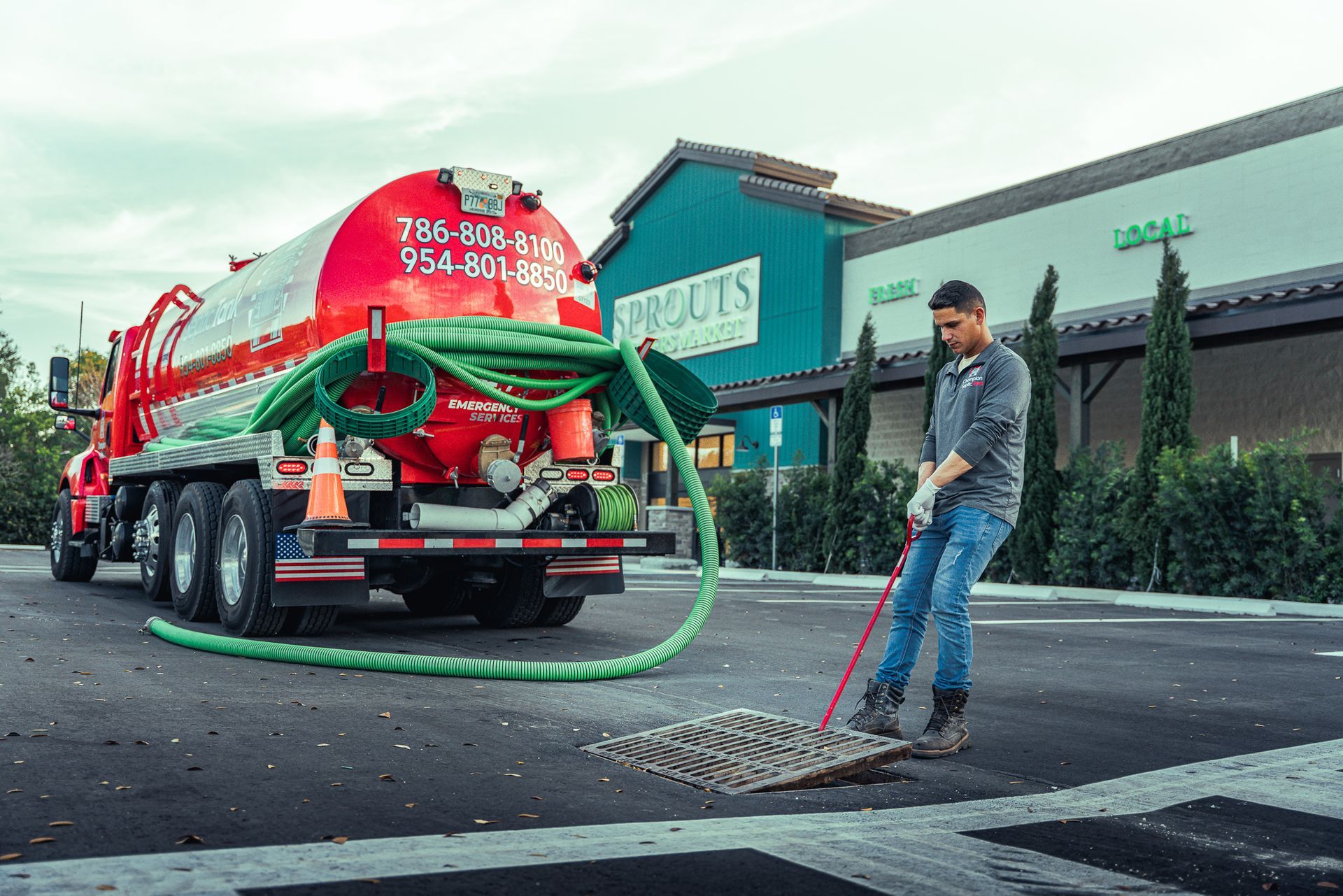 A man is cleaning a manhole cover next to a vacuum truck.