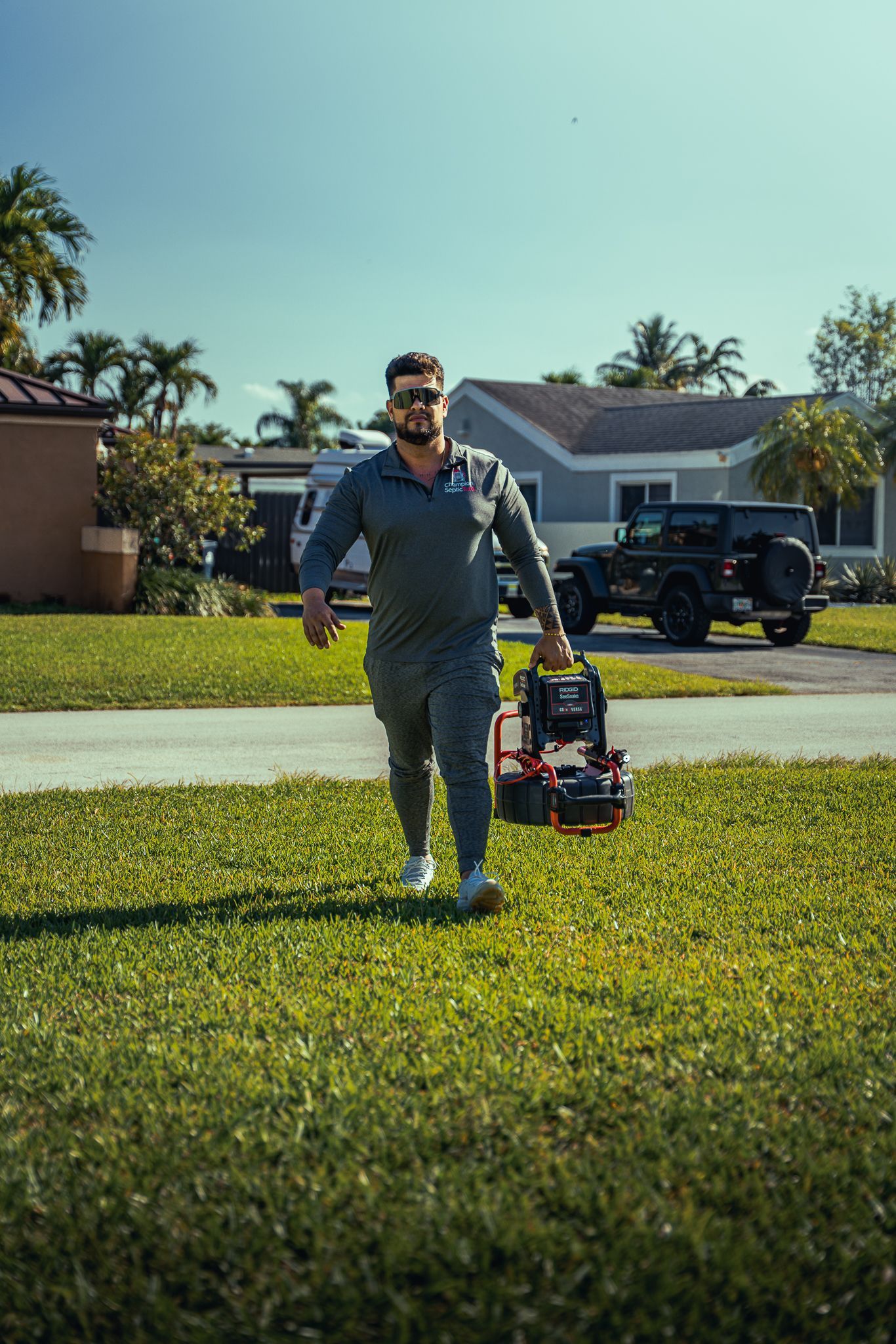 A man is walking through a lush green field carrying a toolbox.