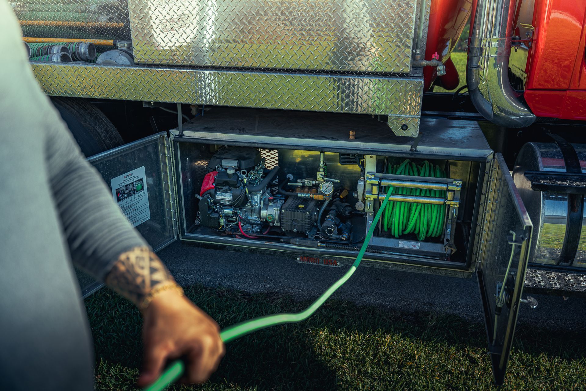 A man is holding a green hose in front of a truck.