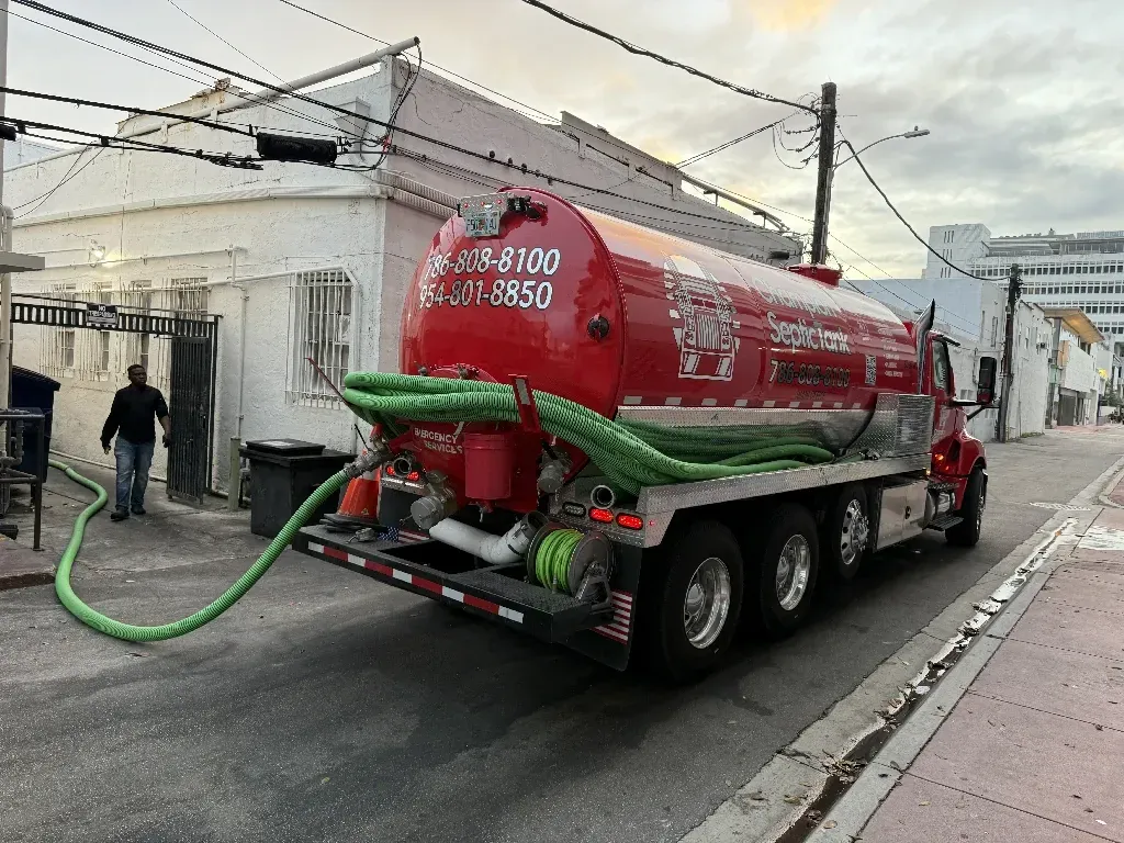 A red septic truck is driving down a city street.