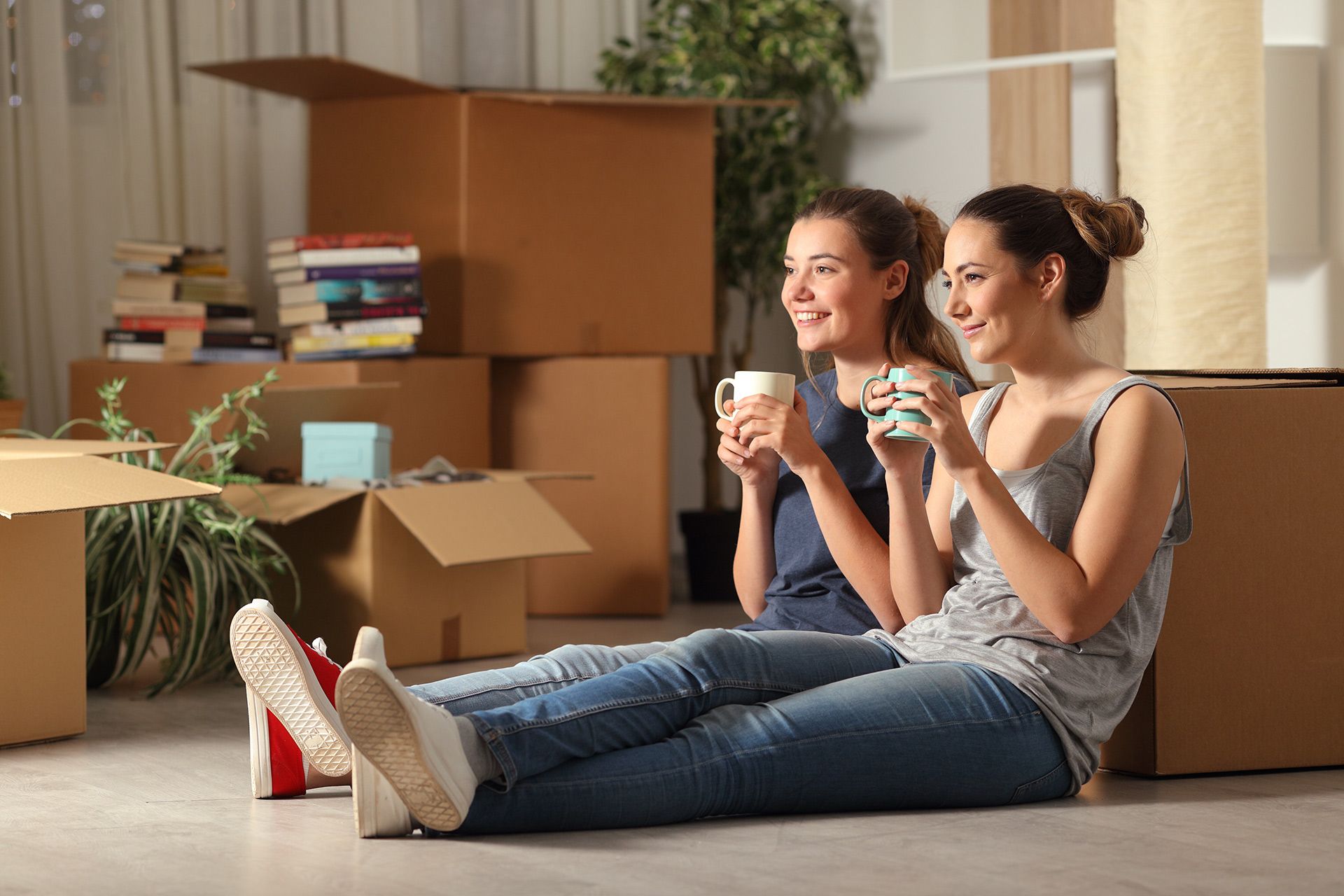 Two people sitting on the floor with coffee among moving boxes in a new home