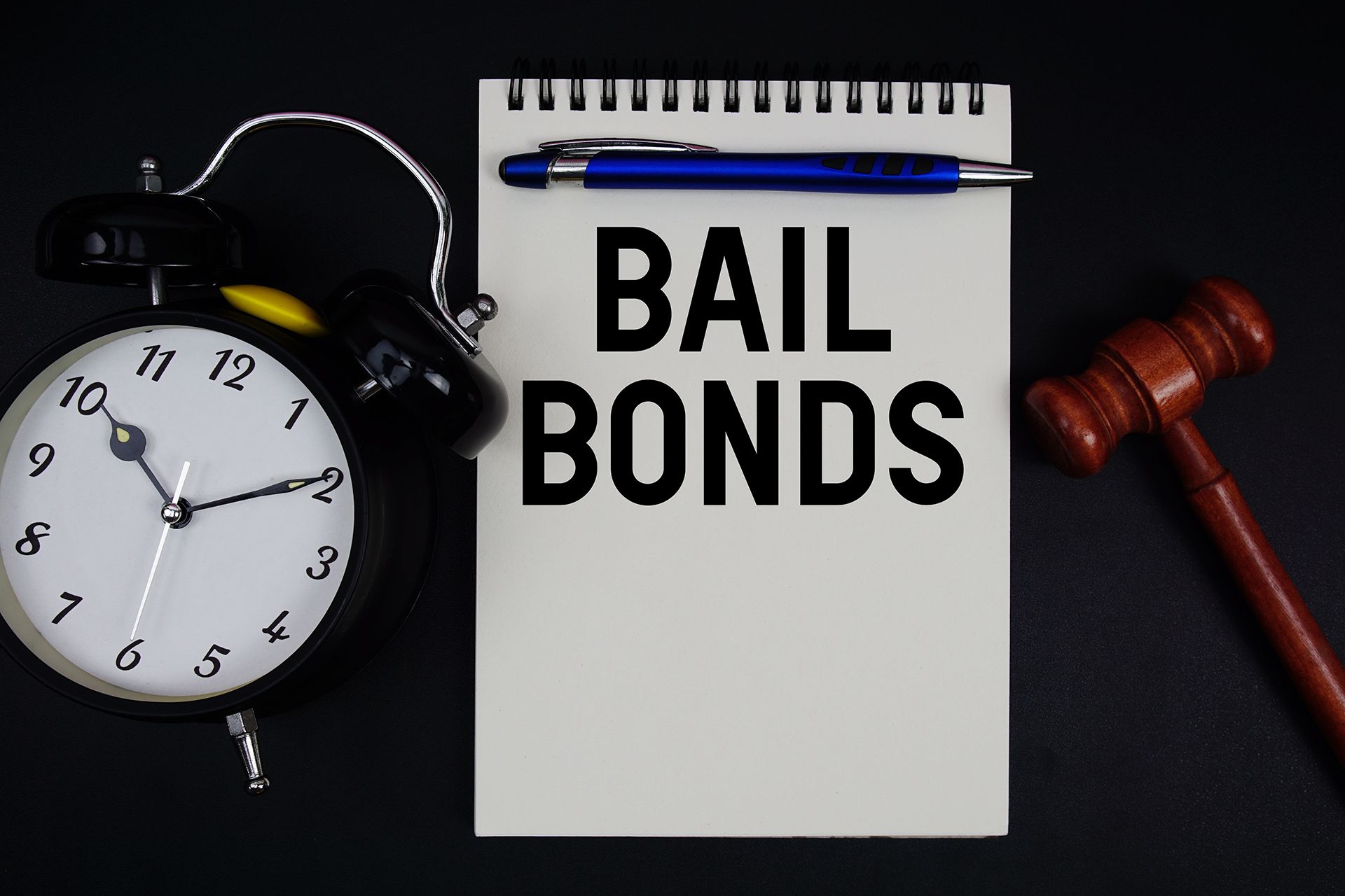 Bail bonds notepad beside alarm clock and gavel on dark background