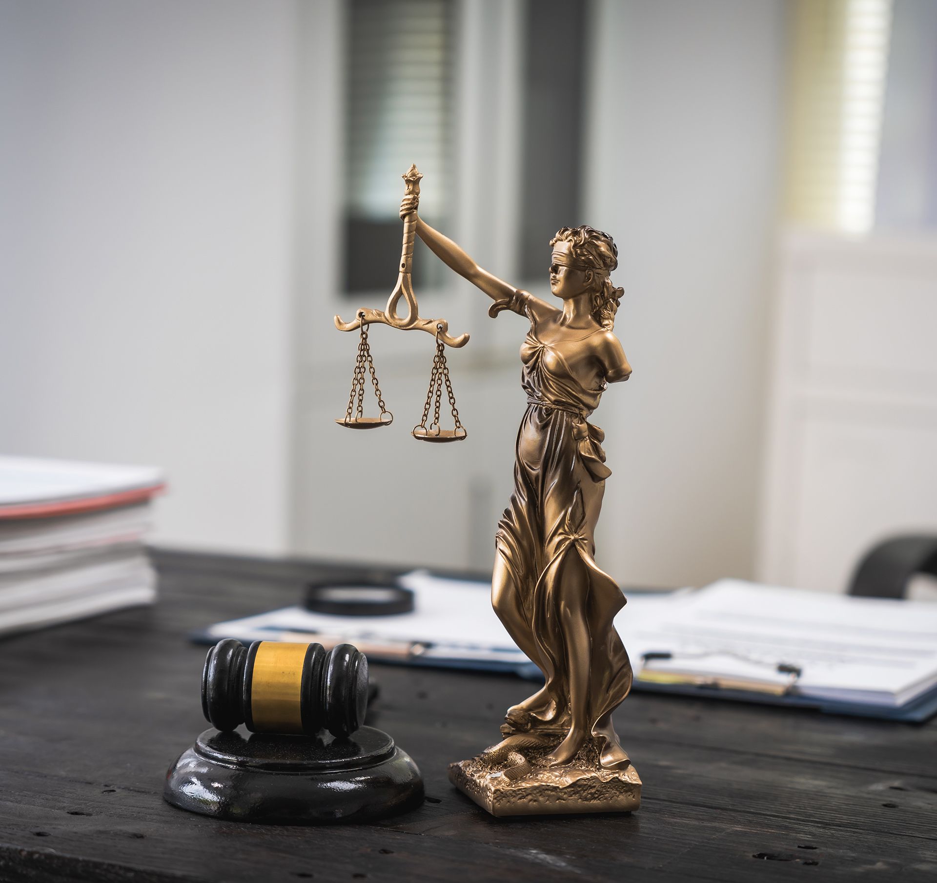 Small gold justice statue holding scales beside a judge’s gavel on a desk in an office.