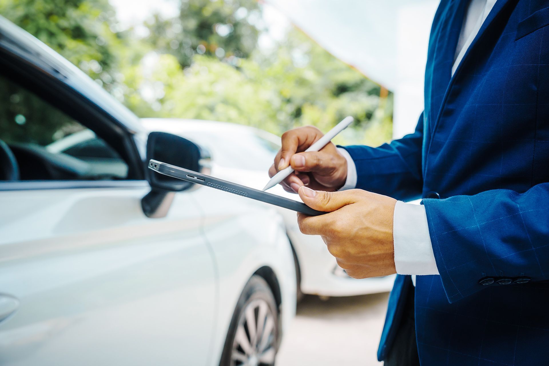 Handing over car keys beside a white car, with a person in a blue suit writing on a clipboard
