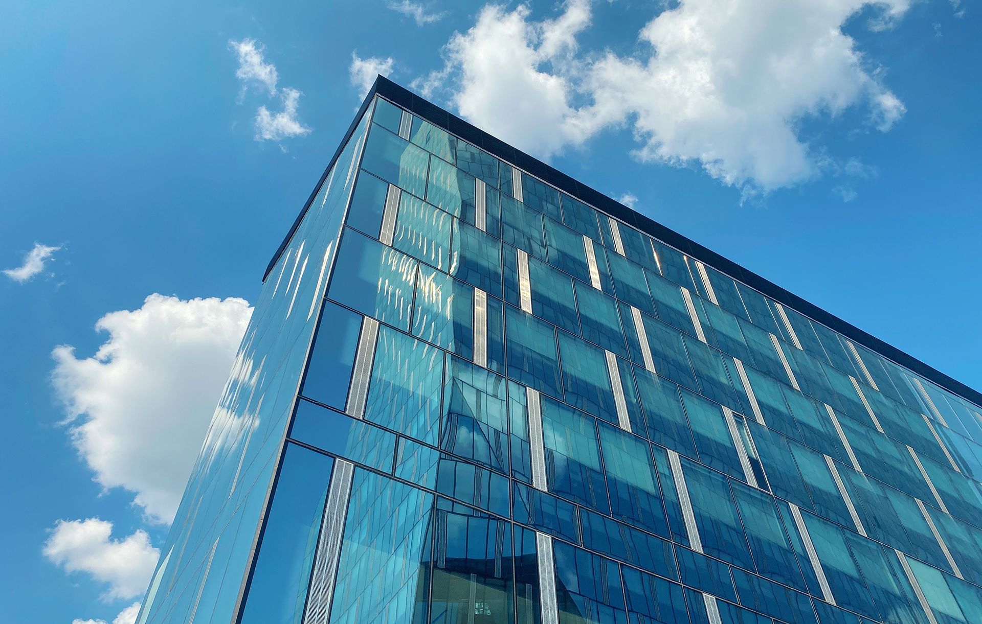 Modern glass office building seen from below against a blue sky with clouds