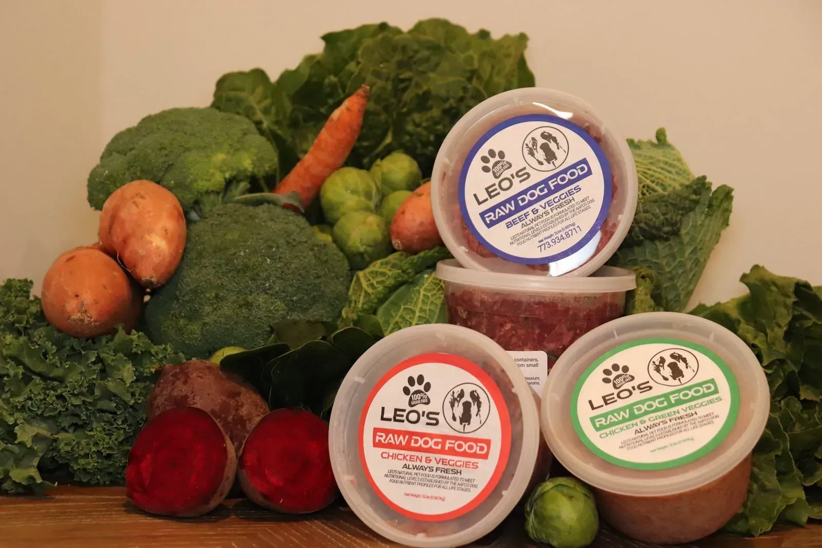 Three tubs of spread with assorted green vegetables and roots arranged behind them on a table