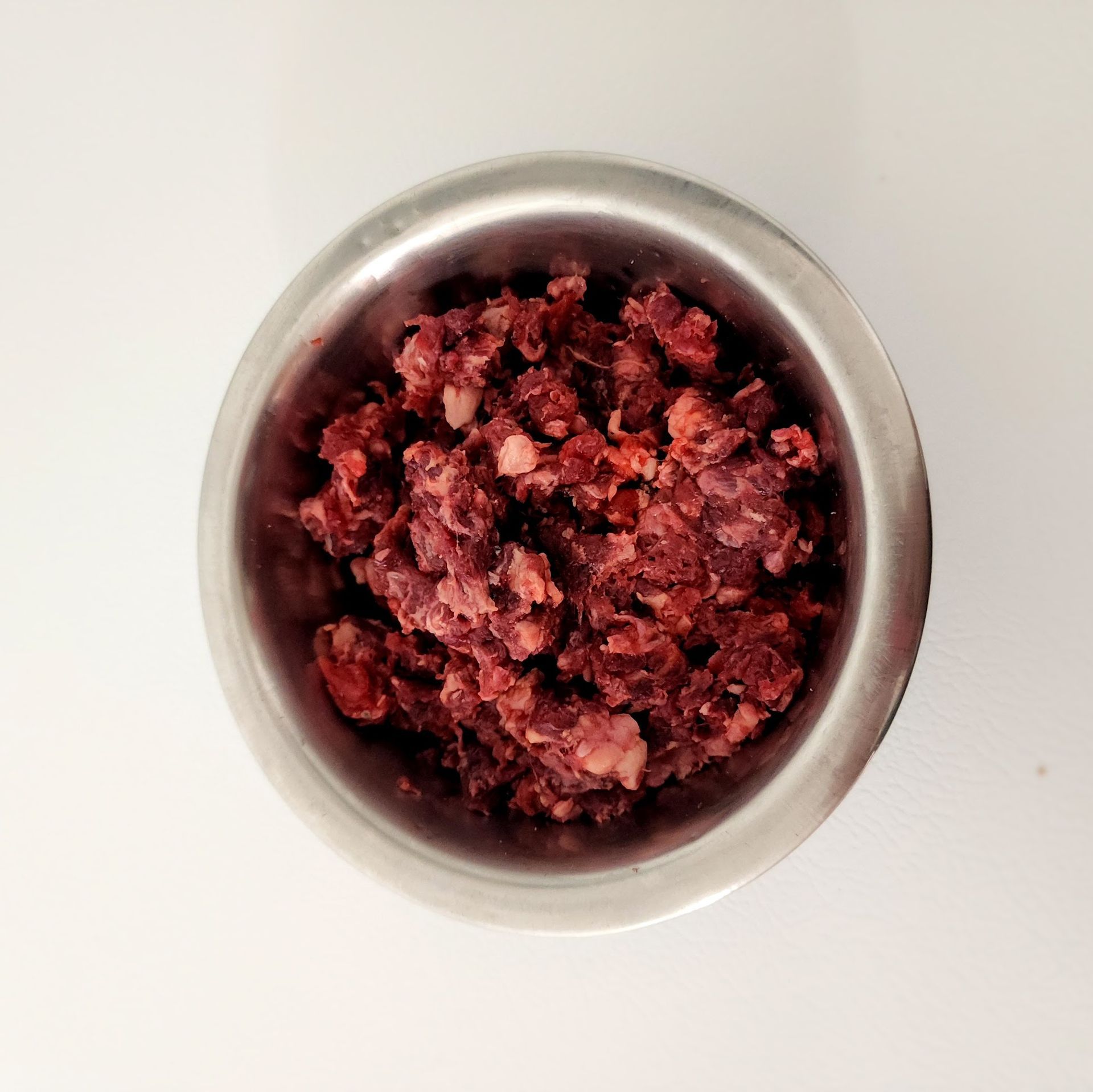 A metal bowl filled with raw, red ground meat on a white surface.