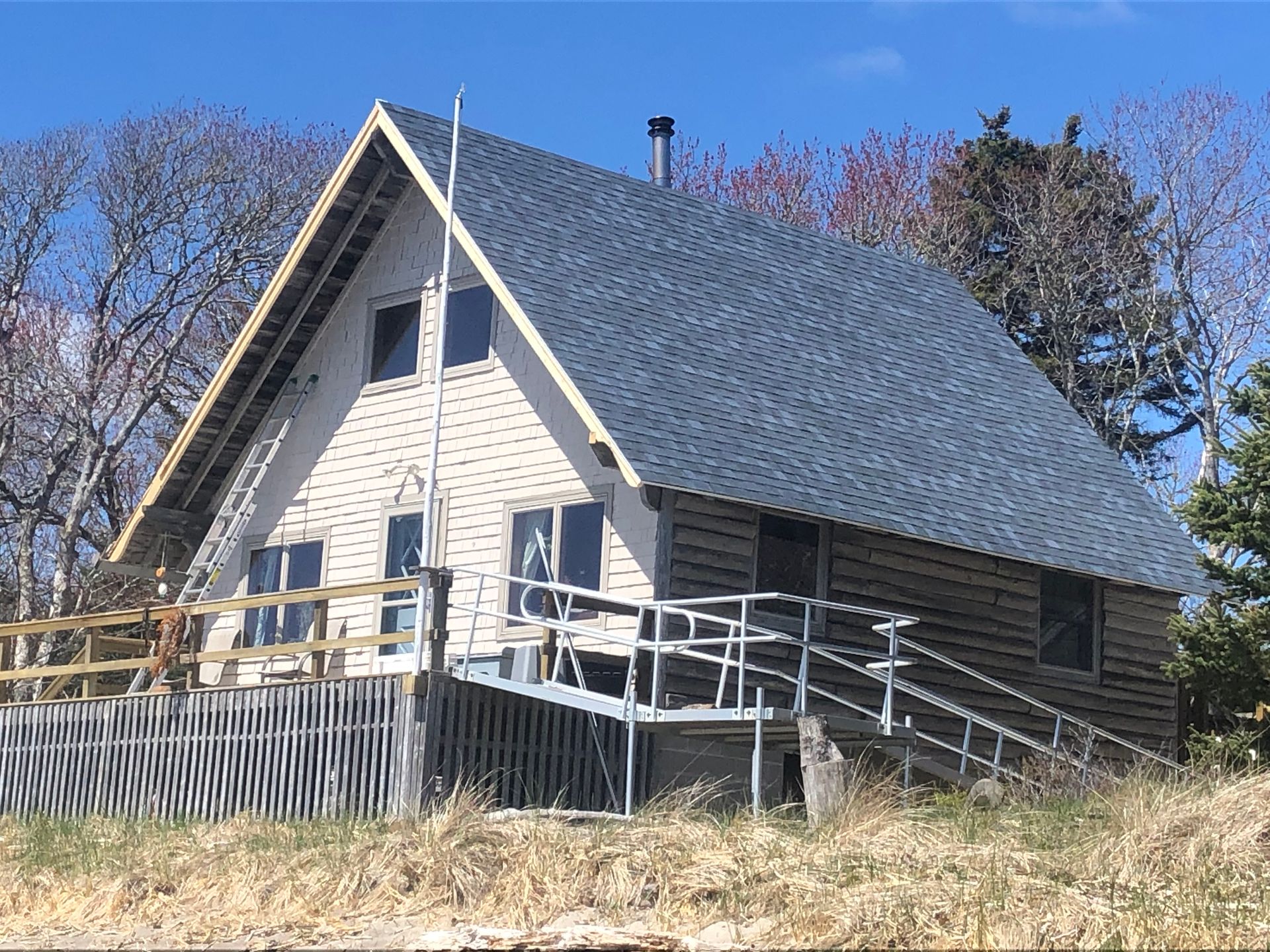 A white house with a gray roof is sitting on top of a grassy hill.
