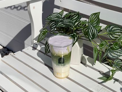 Iced drink in a clear cup on a white patio table beside a leafy potted plant and railing.