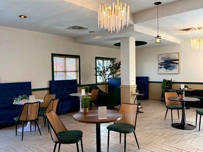 Modern lounge with blue booths, wicker chairs, tables, and a chandelier in a bright, airy room