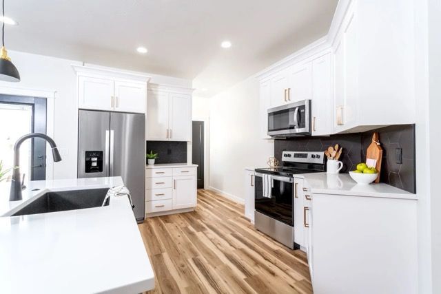 A kitchen with white countertops, cabinetry, and walls with wood floors