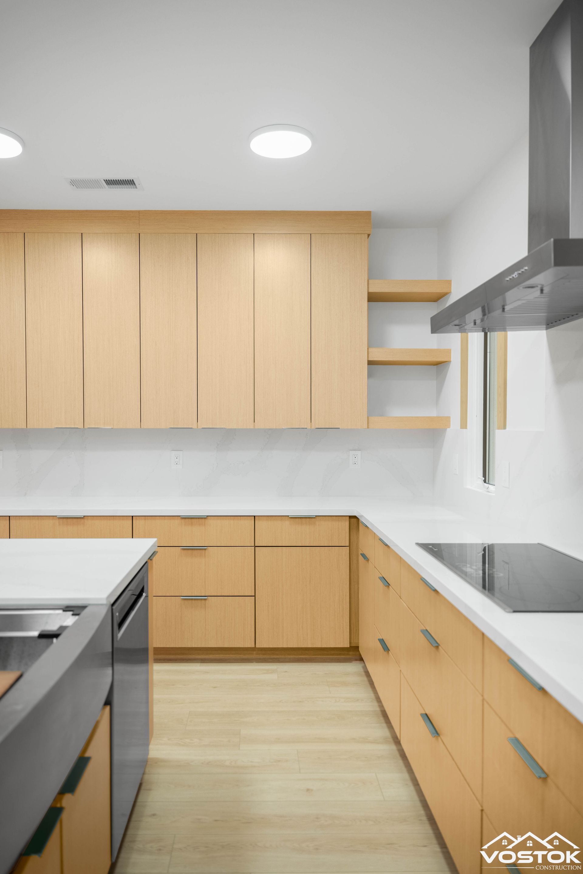 Modern kitchen with light wood cabinets, white countertops, stainless range hood, and recessed lighting