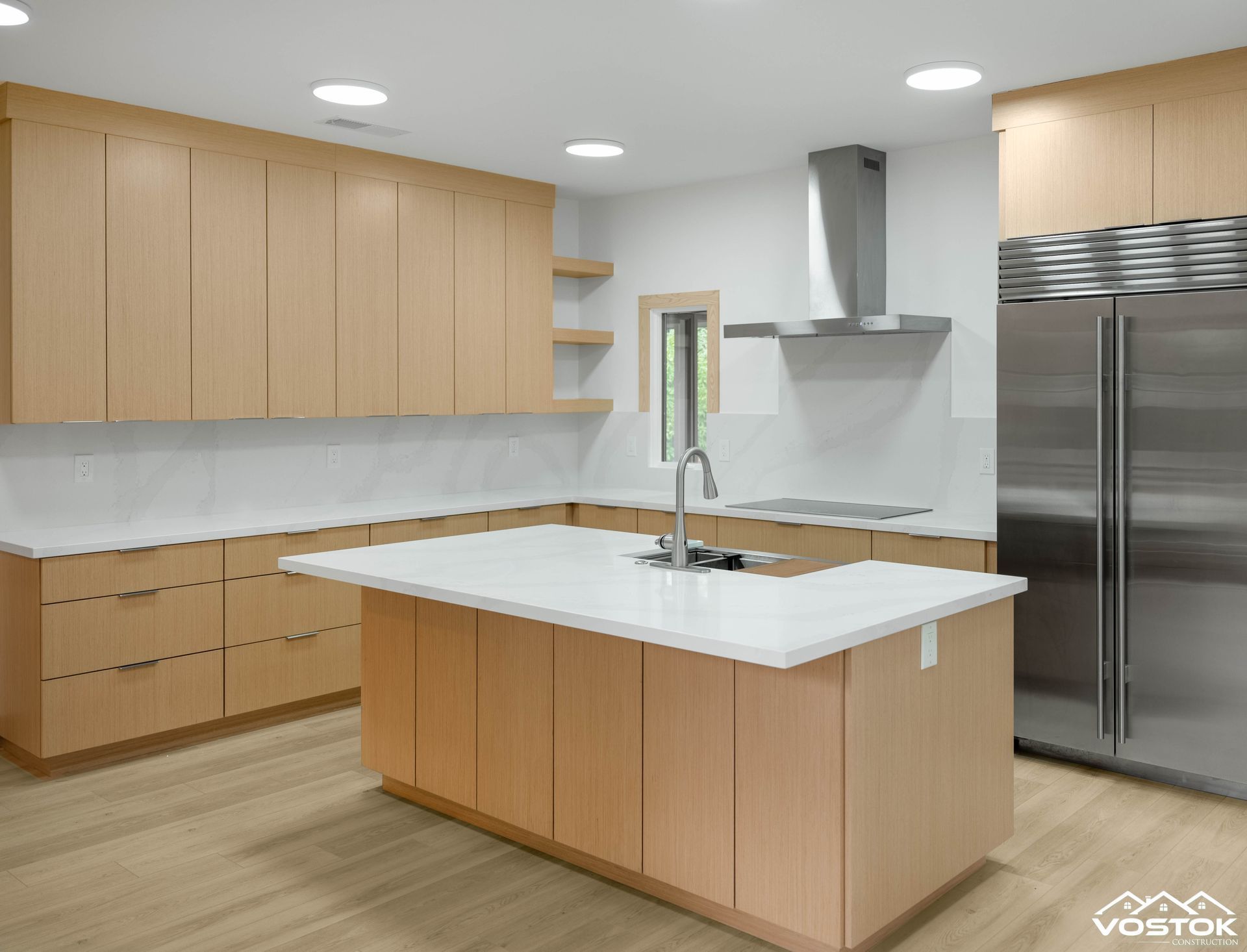 Contemporary kitchen with light wood cabinets, white countertops, stainless appliances, and center island