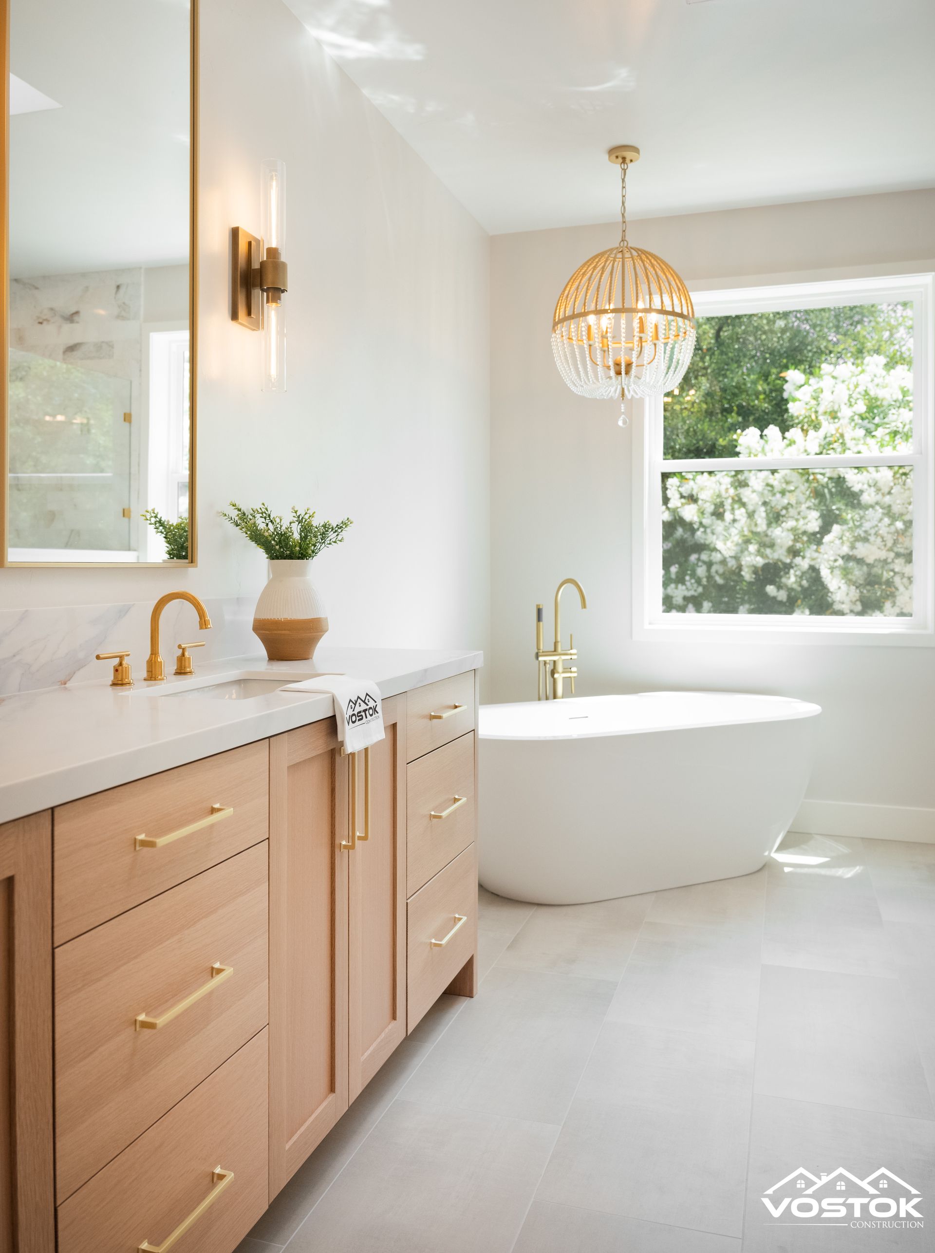 Elegant bathroom with freestanding tub, wood vanity, gold fixtures, and spherical chandelier