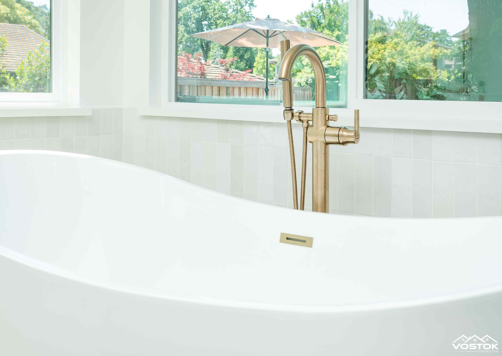A white bathtub with a gold faucet in a bathroom next to a window.