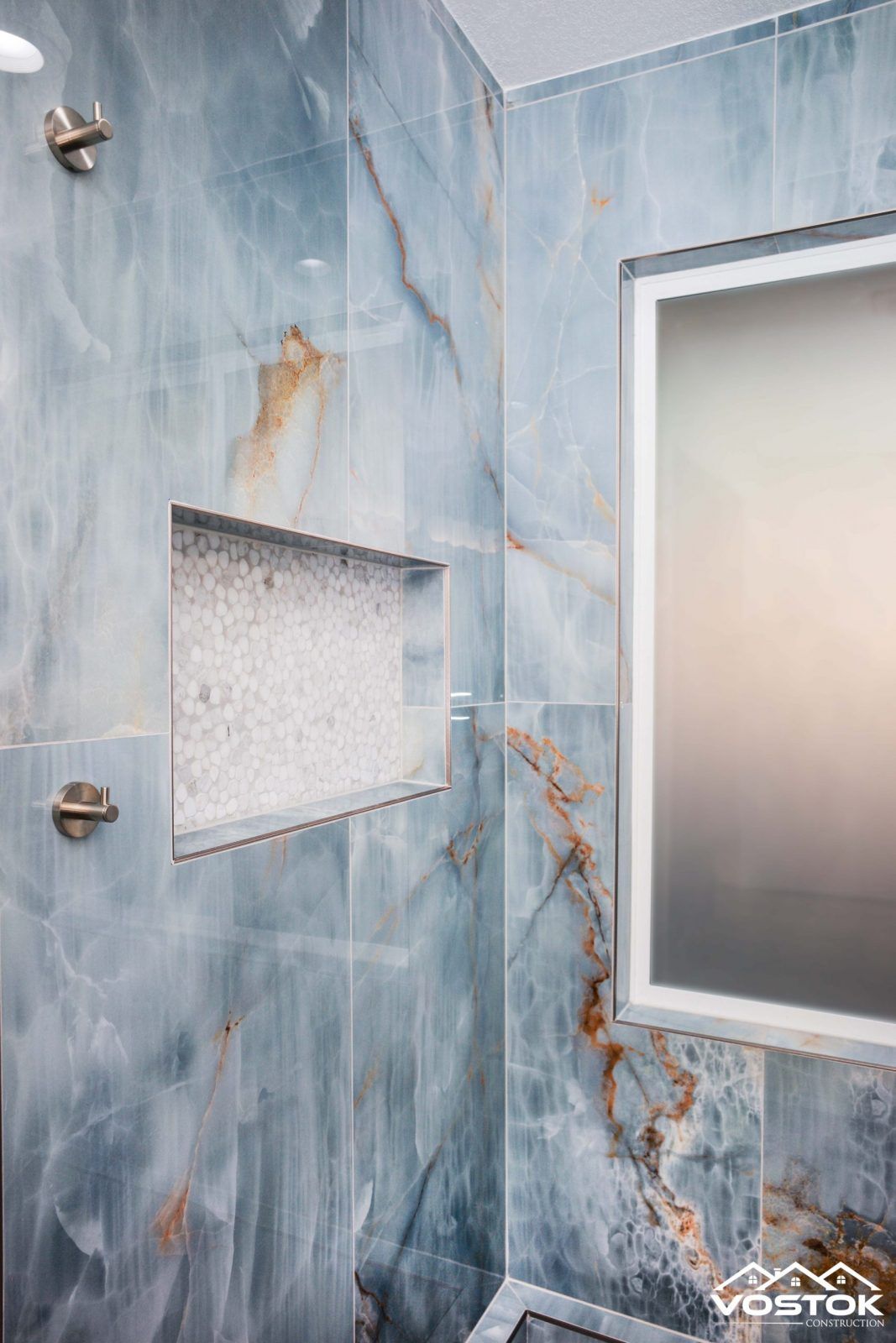 A bathroom with blue tiles , a shower , and a mirror.