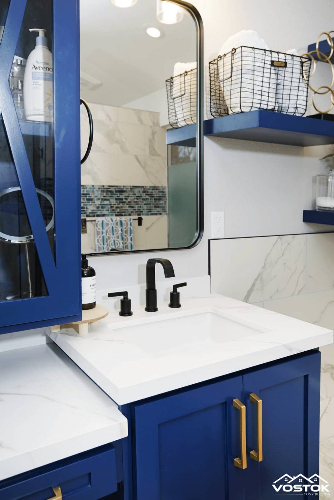 A bathroom with blue cabinets , a sink , a mirror and shelves.