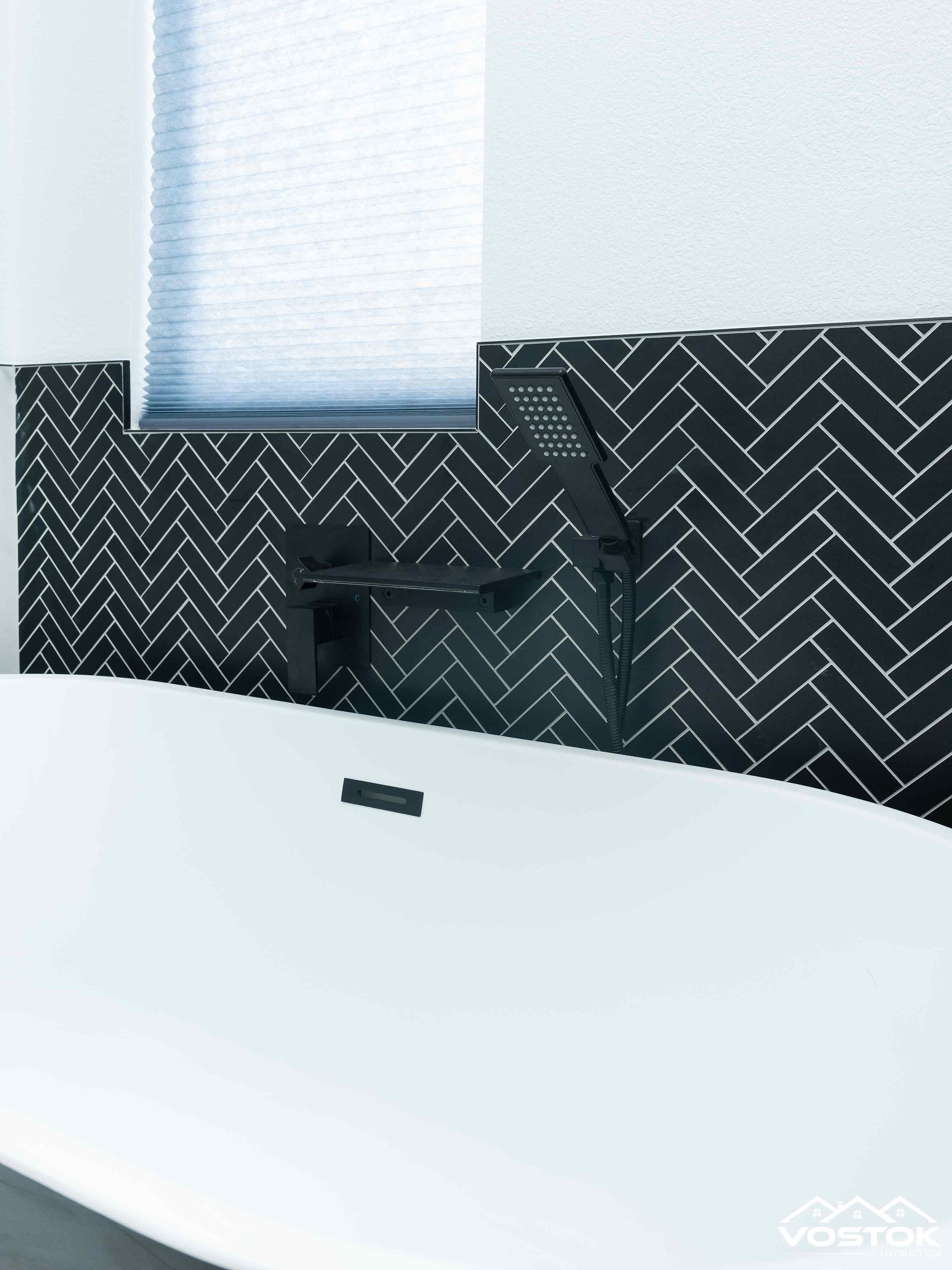 A bathtub in a bathroom with black herringbone tiles