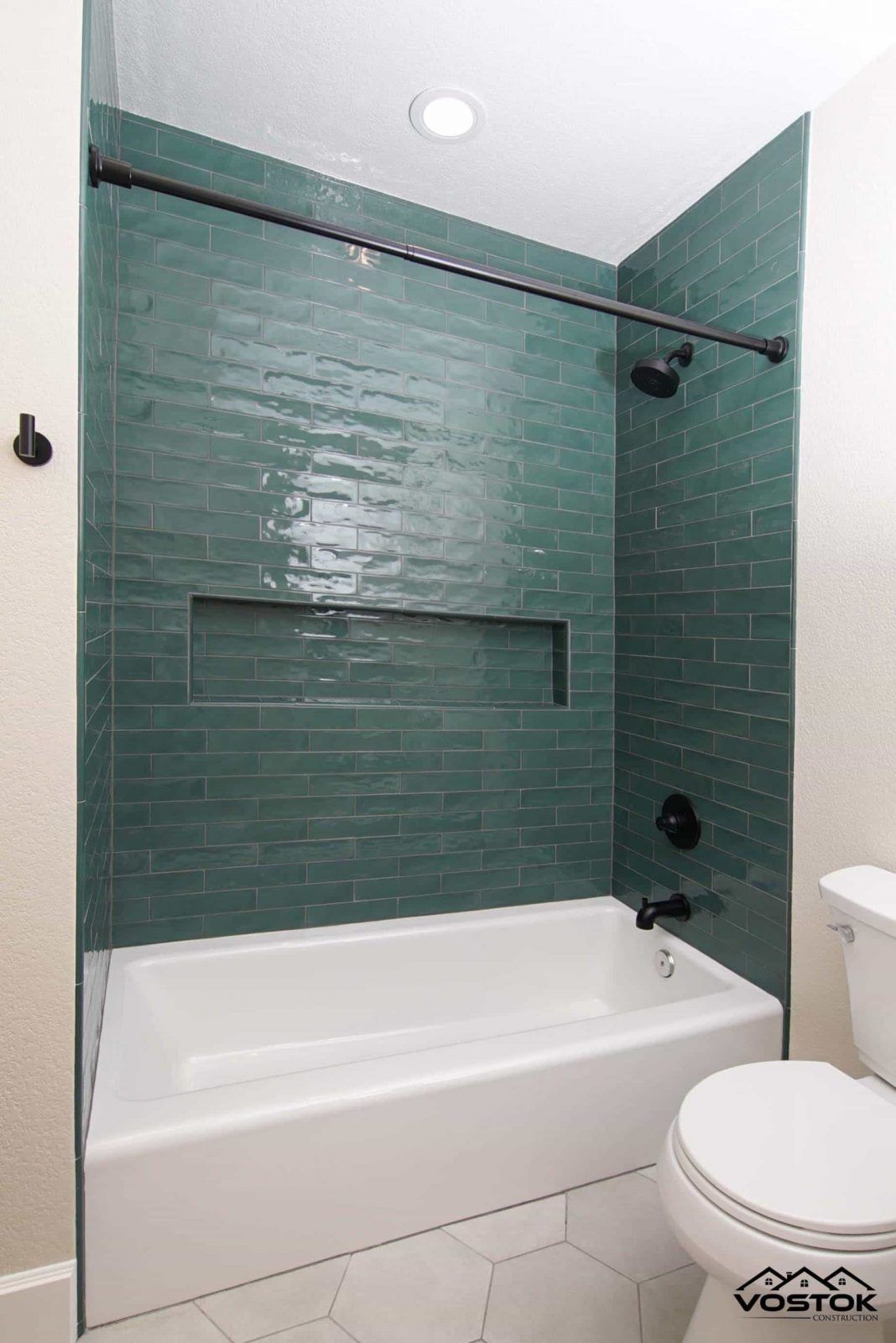 A bathroom with a bathtub , toilet and green tiles.