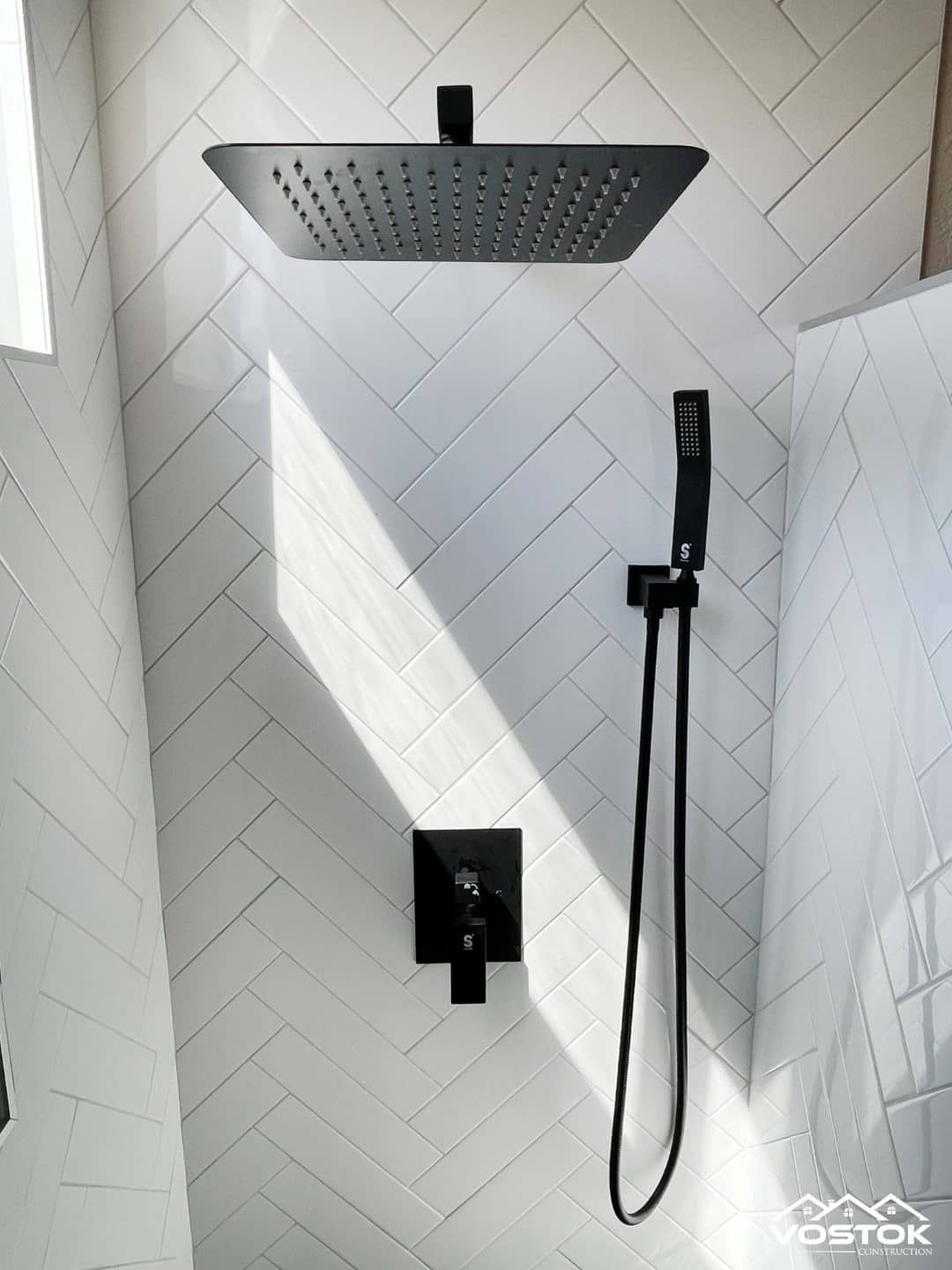 A black shower head is hanging from a white tiled wall.
