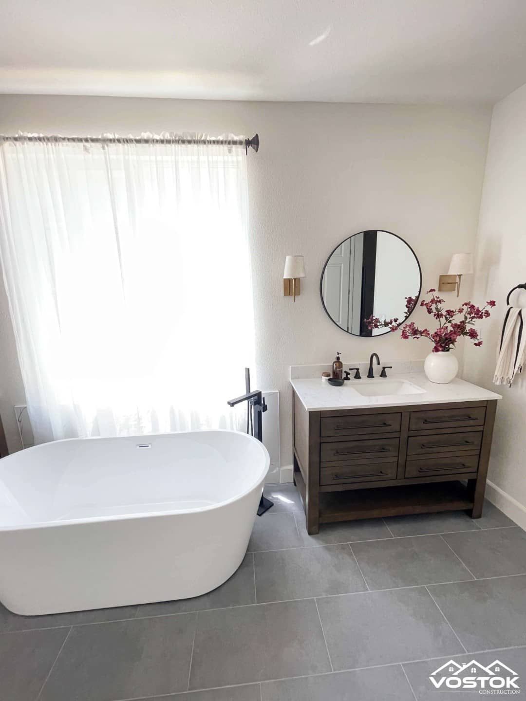 A bathroom with a bathtub , sink , mirror and window.