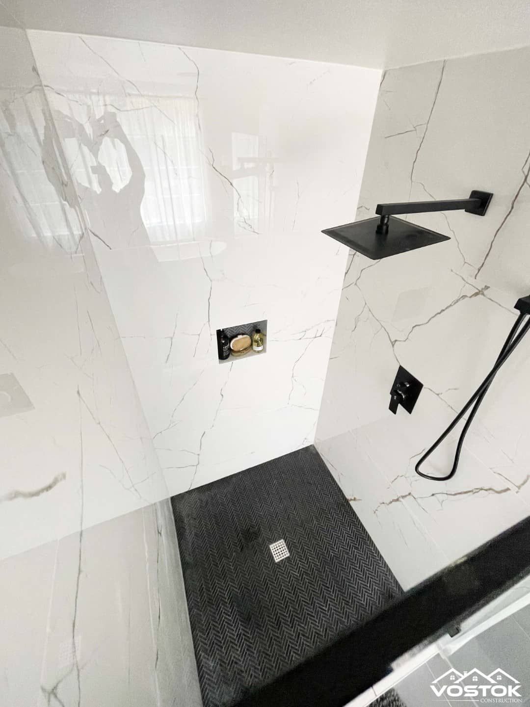 A bathroom with a walk in shower and a black shower head.