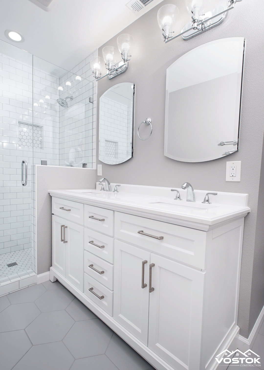 A bathroom with two sinks , two mirrors , and a walk in shower.