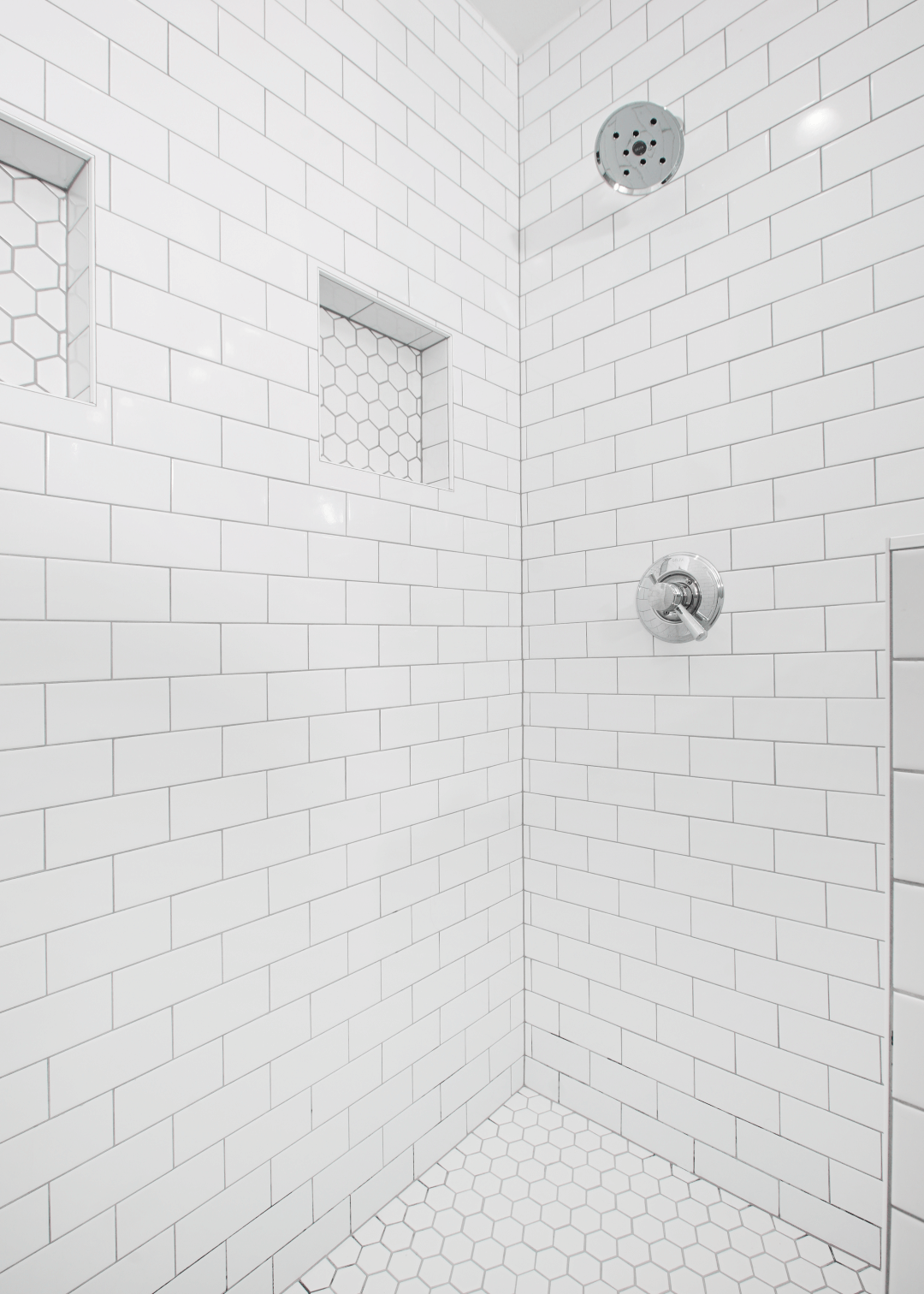 A shower with white tiles and a shower head.