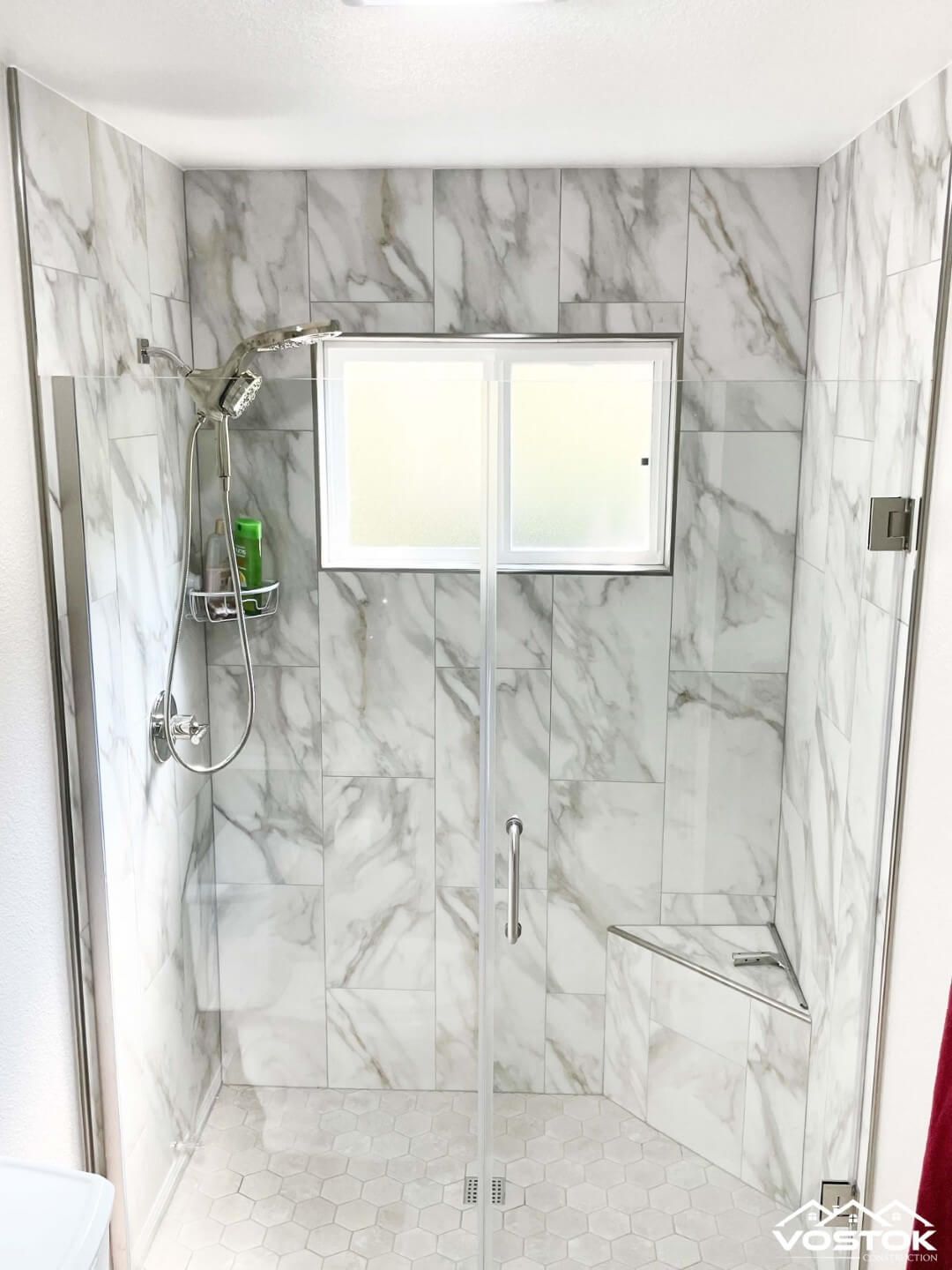 A bathroom with marble tiles and a walk in shower with a window.