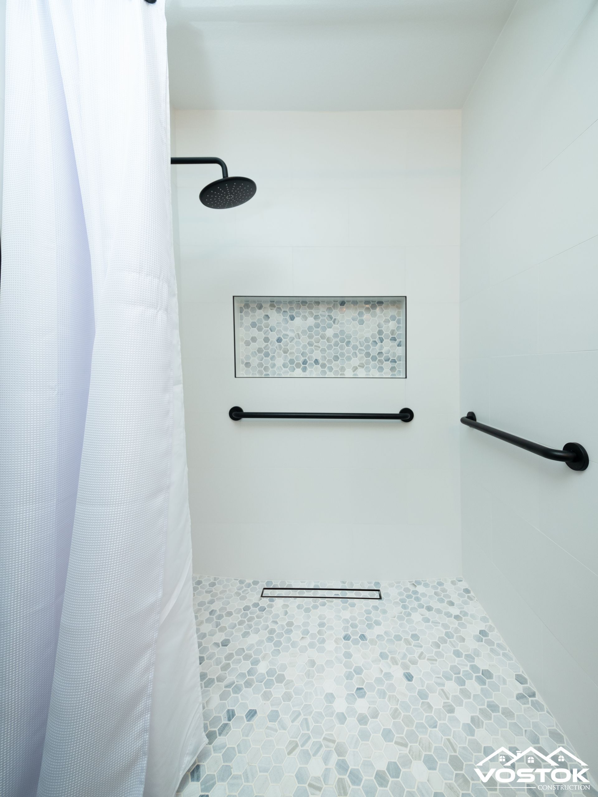 A shower with a white shower curtain and a black shower head.