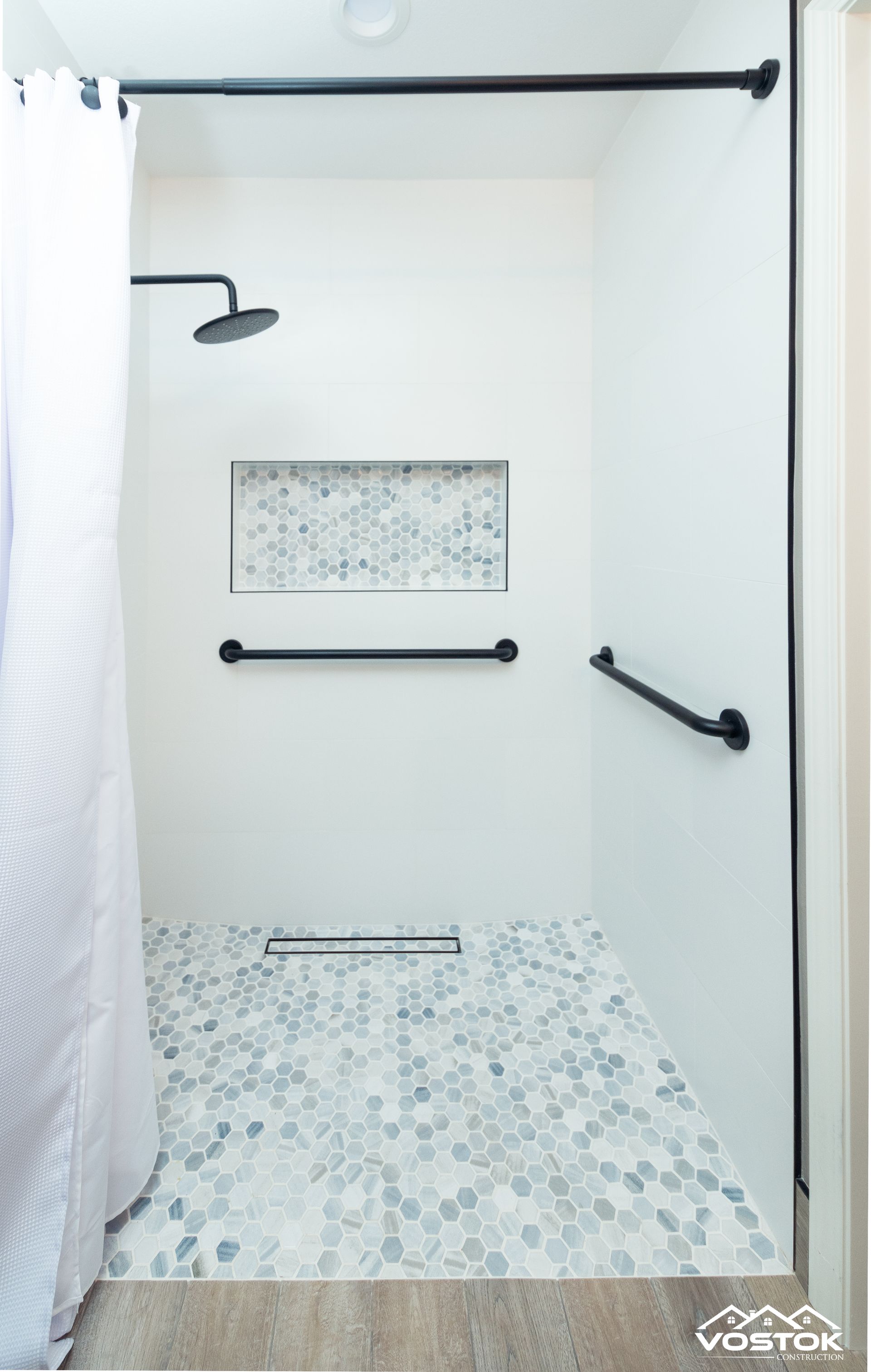 A bathroom with a walk in shower with handrails and a shower head.