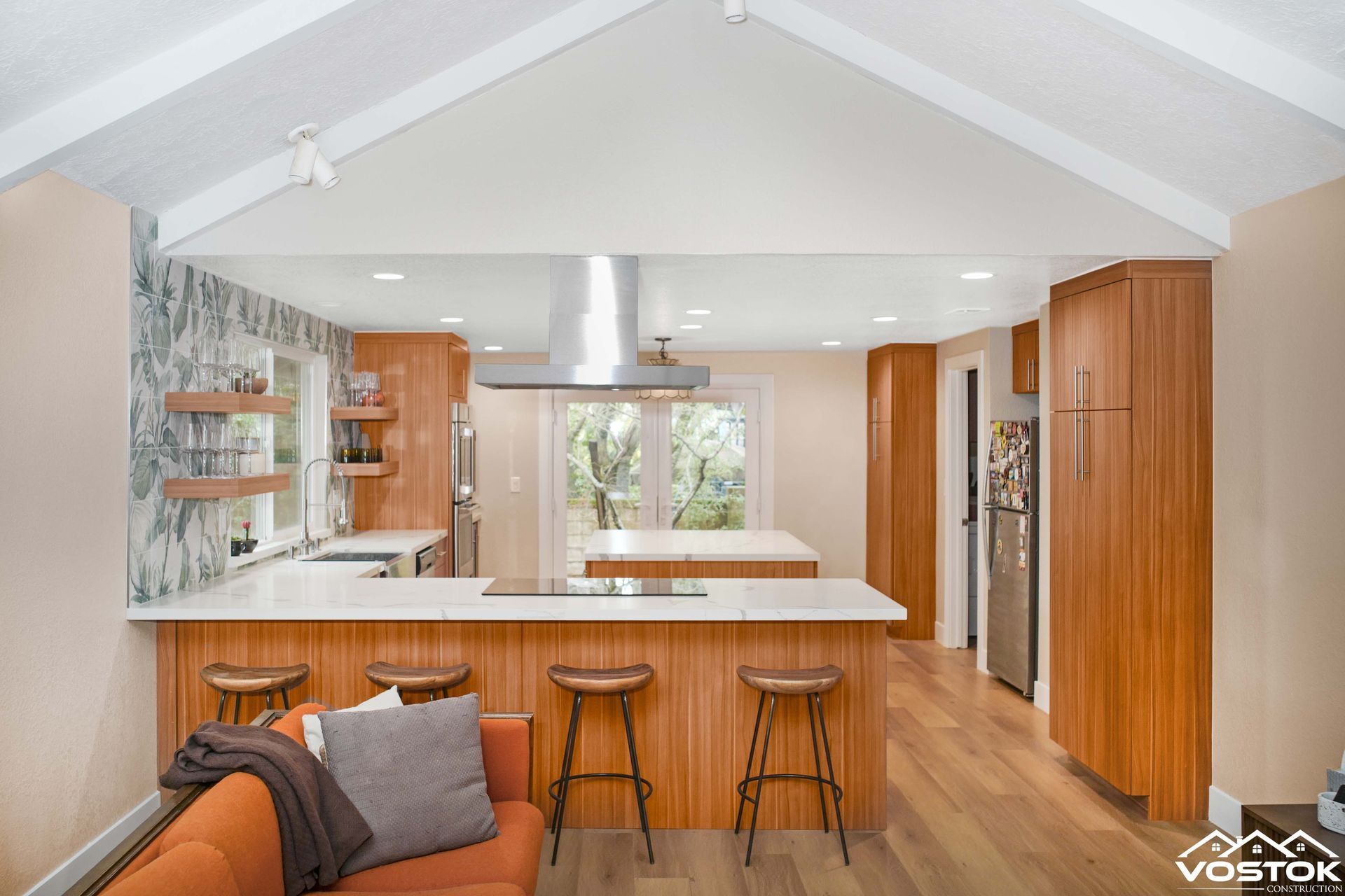 A living room with a couch , stools , and a kitchen.