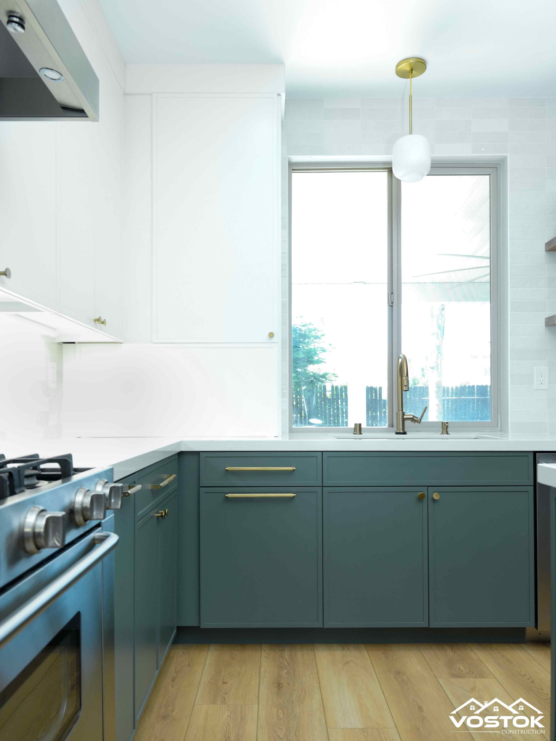 A kitchen with blue cabinets , a stove , a sink and a window.