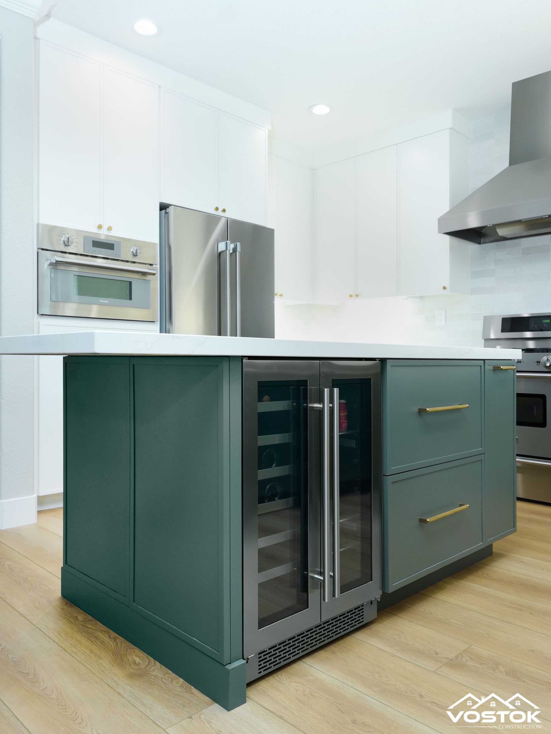 A kitchen with a green island , stainless steel appliances , a refrigerator and a wine cooler.