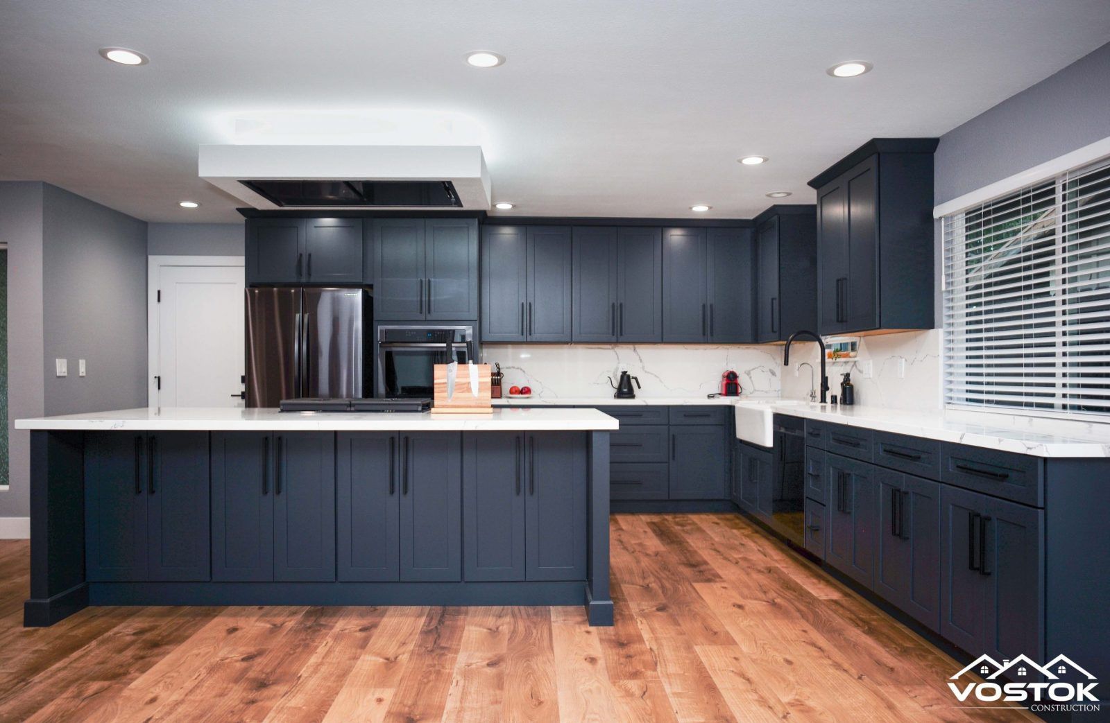 A kitchen with blue cabinets , white counter tops , and a large island.
