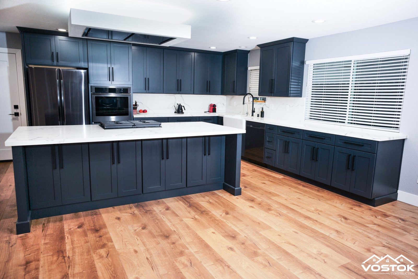 A kitchen with blue cabinets , white counter tops , and a large island.