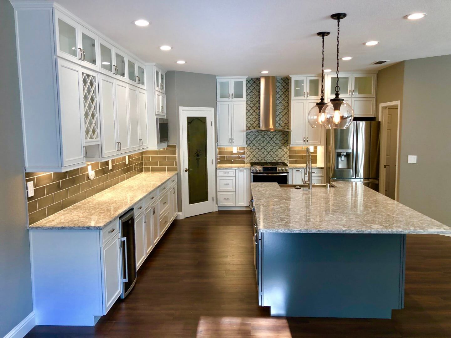 A kitchen with white cabinets , granite counter tops , stainless steel appliances and a large island.