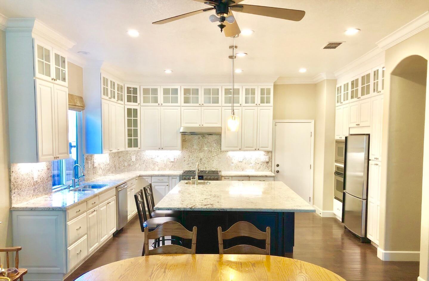 A kitchen with white cabinets , granite counter tops , stainless steel appliances and a ceiling fan.