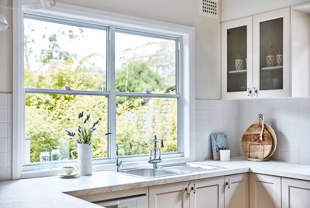 A kitchen with white cabinets , a sink , and a window.