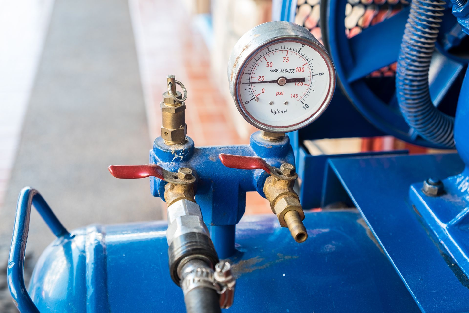 Commercial air compressor repair view showing a pressure gauge, valves, and blue tank. 