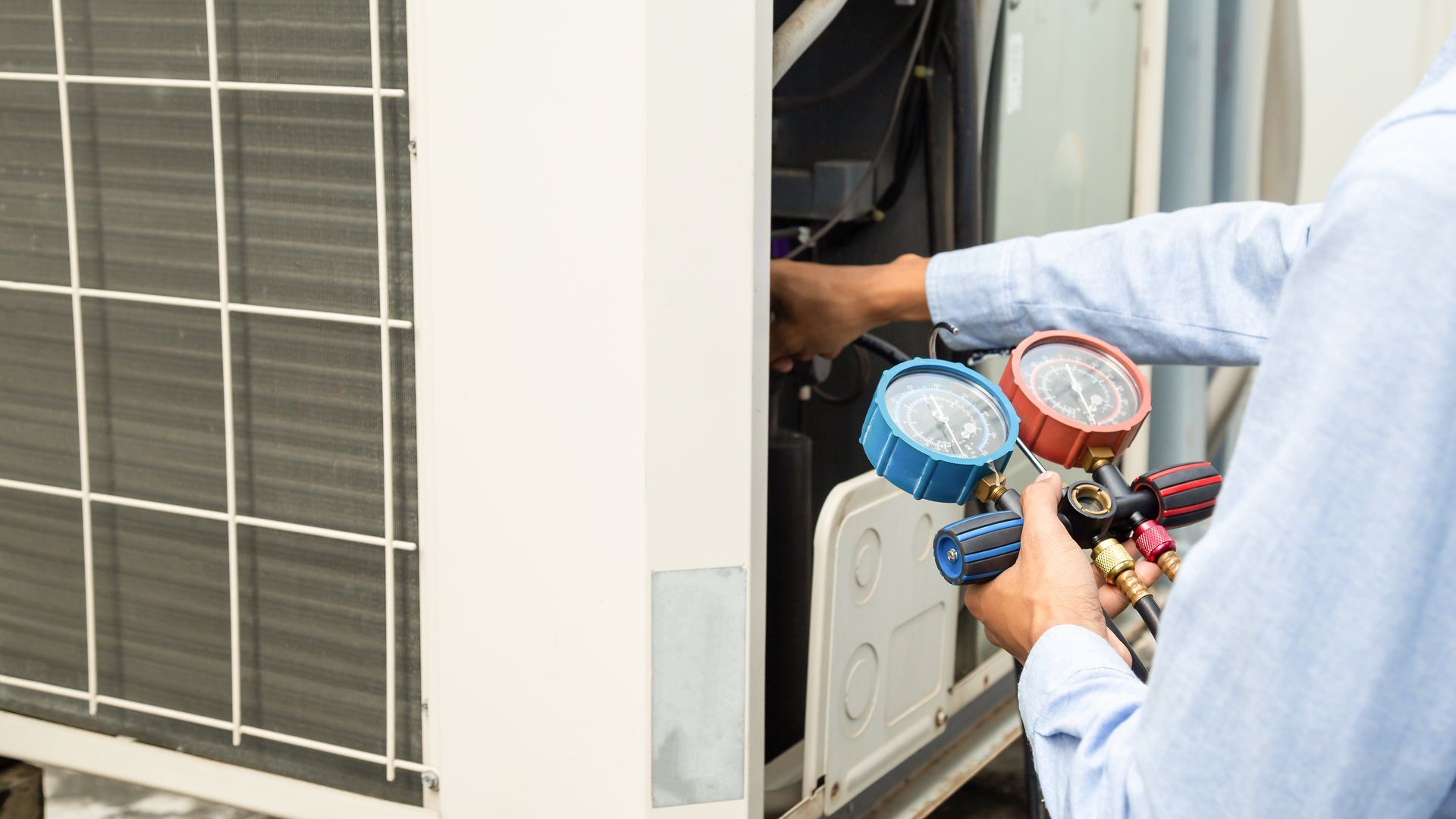 a technician using a manifold gauge set to check pressure on an air conditioning unit.