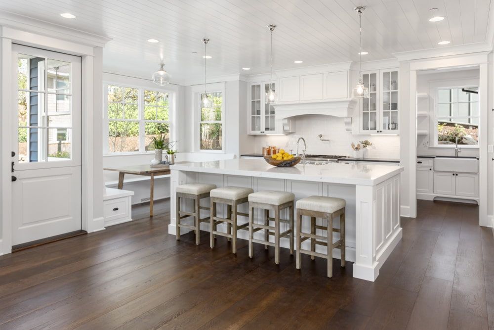 A Kitchen With White Cabinets, Hardwood Floors, A Large Island And Stools — South East Kitchens In Burleigh Heads, QLD