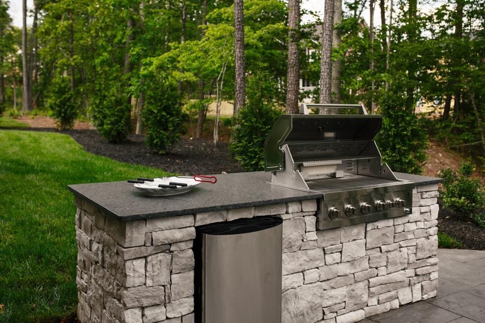 A Grill Is Sitting On Top Of A Stone Counter Next To A Trash Can — South East Kitchens In Burleigh Heads, QLD